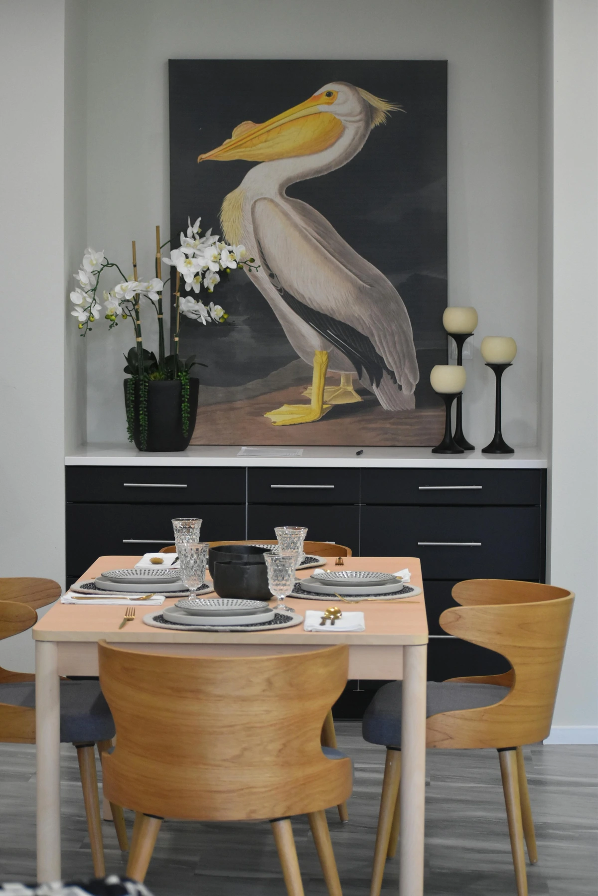 Painting of a pelican above a modern dining room table set for a meal.