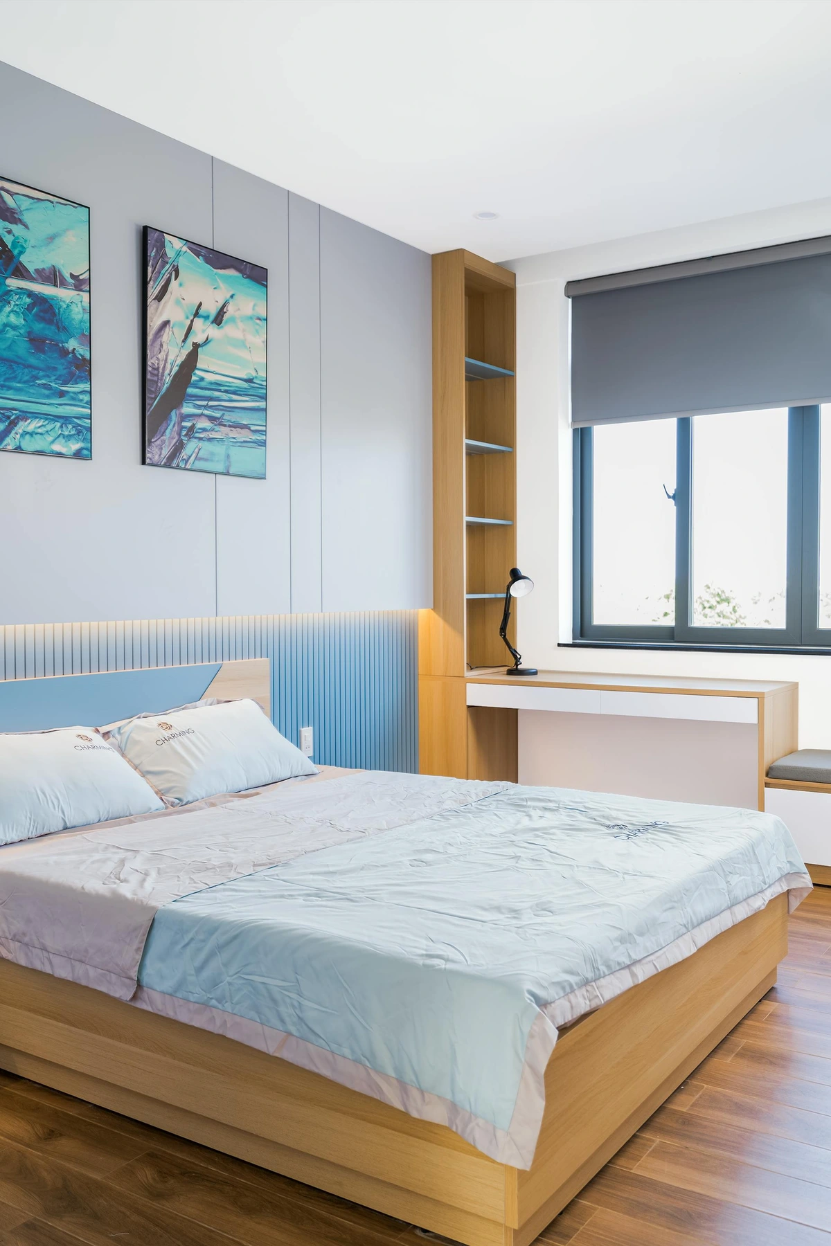 Modern bedroom design for a teenager featuring a bed with blue bedding, abstract wall art, and a wooden desk with shelving.