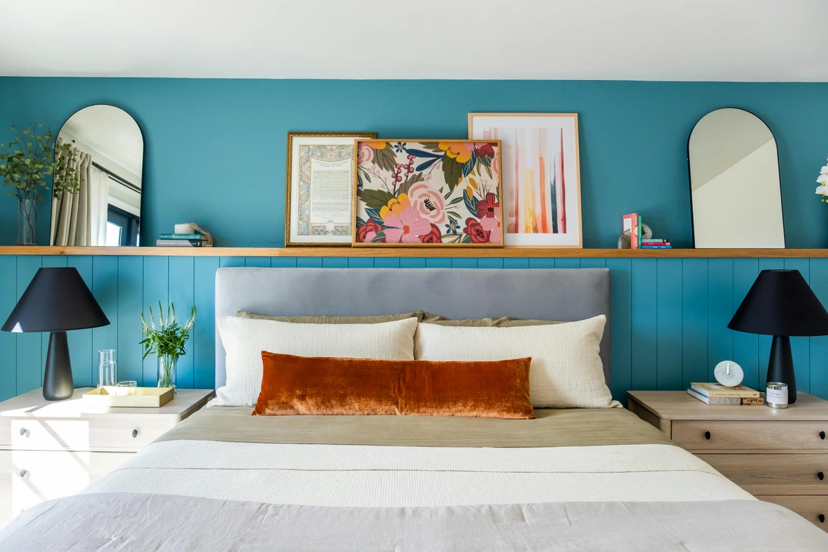 Bedroom interior with teal walls, a grey headboard, and curated wall art above the bed.