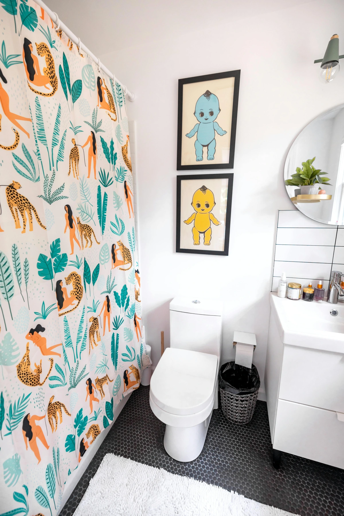 Modern bathroom interior with a unique shower curtain featuring leopards and female figures, framed art, and a vanity with a mirror.
