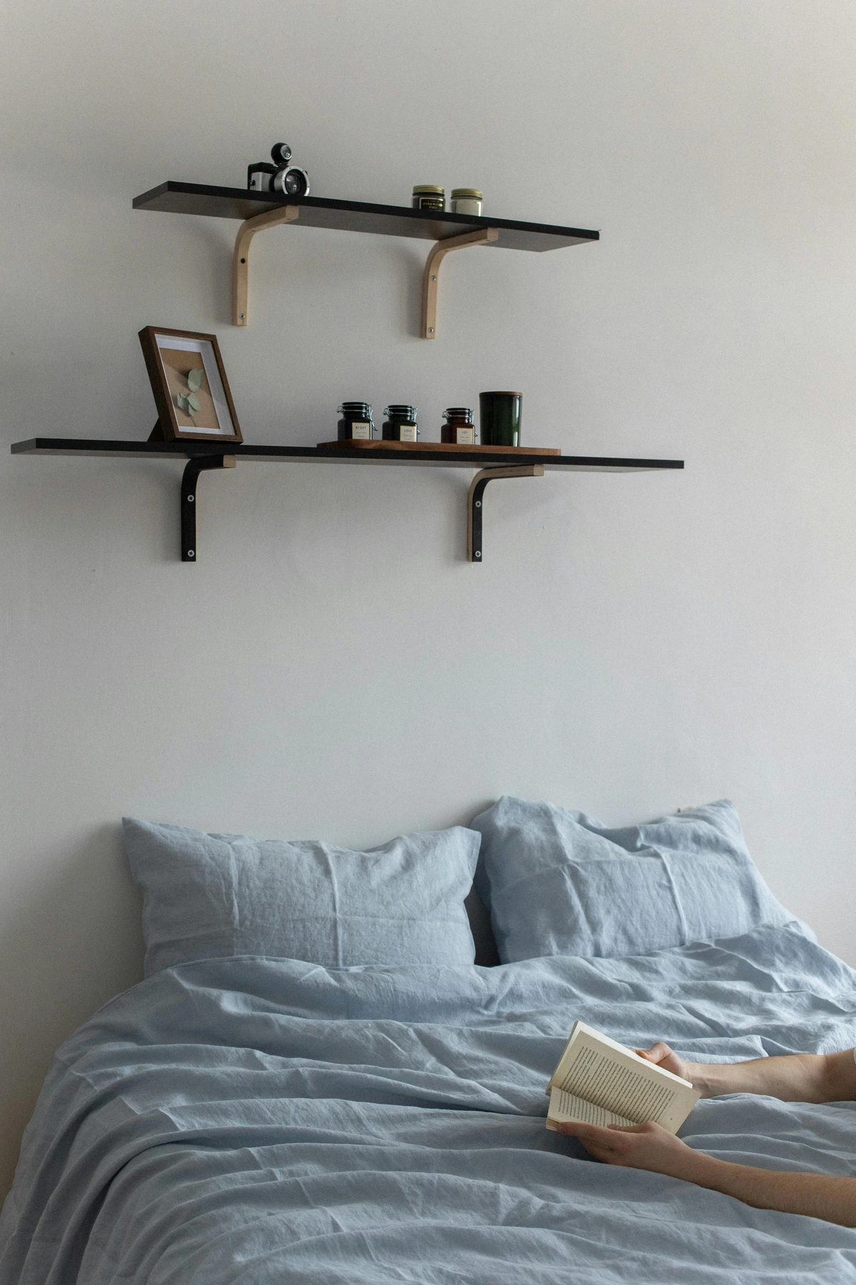 Stylish shelves decorated with jars, a picture frame, and a candle, mounted above a neatly made bed with light blue linen bedding.