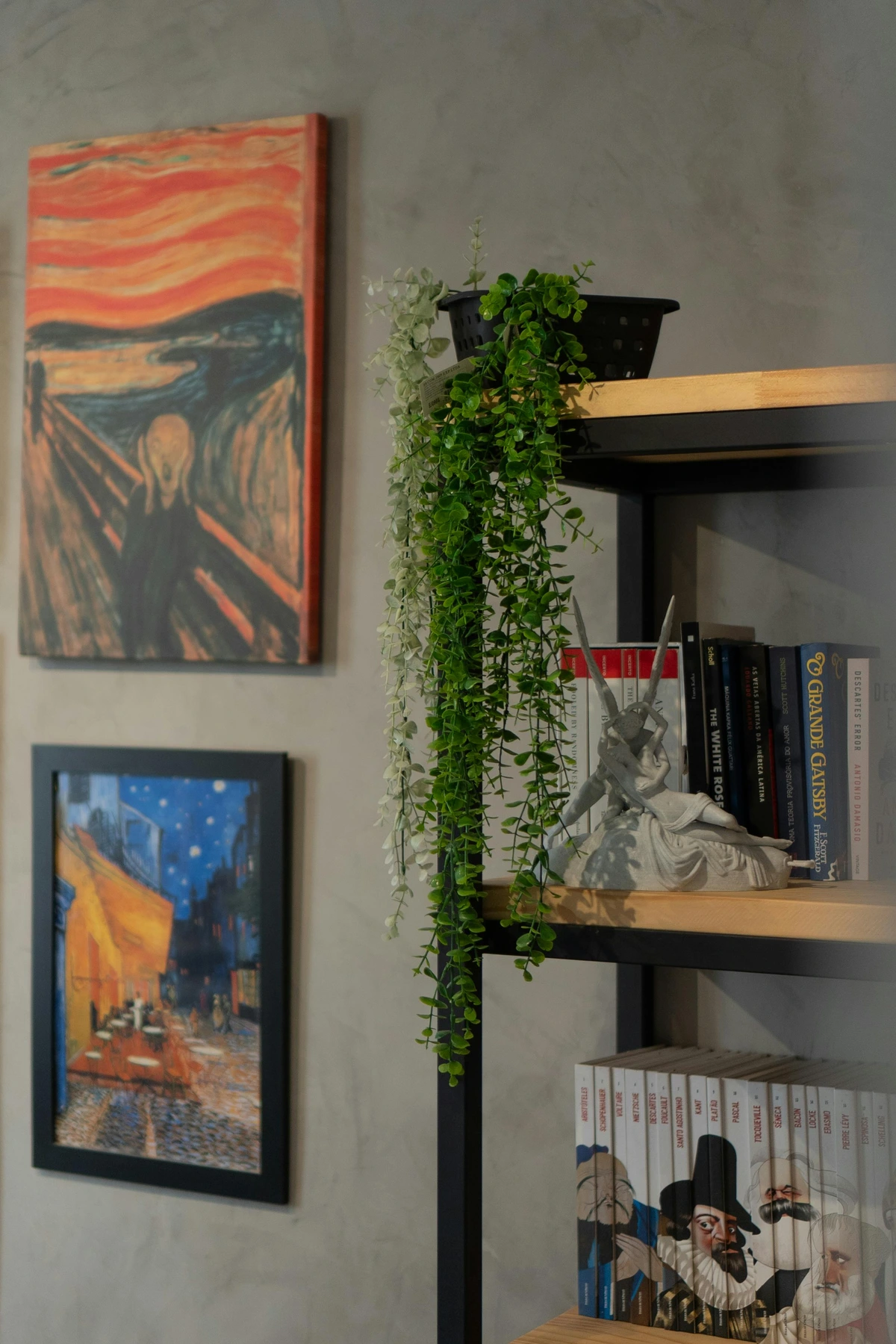 Paintings displayed on a wall next to a bookshelf filled with books and decorative items.