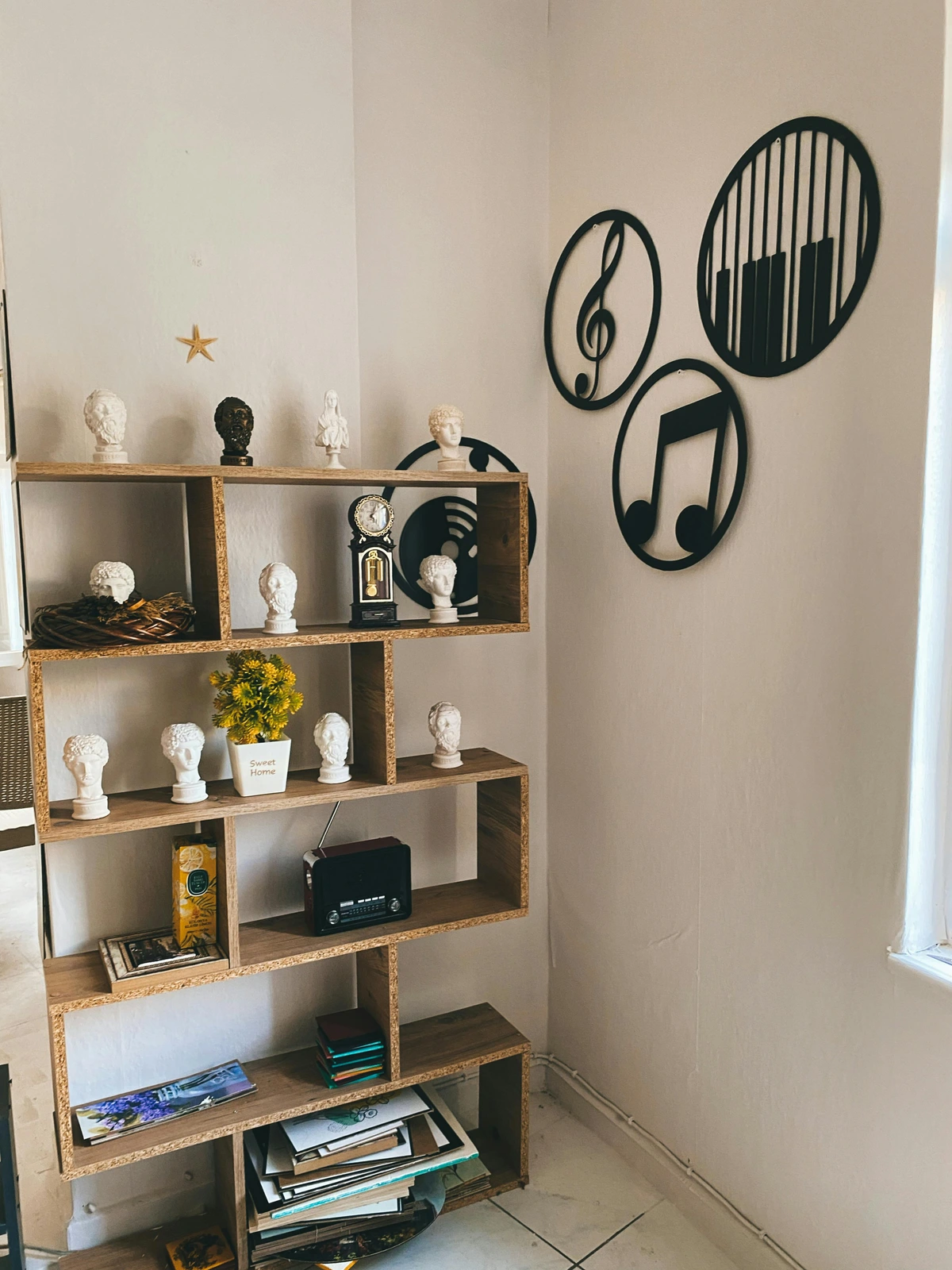 Wooden bookshelf displaying various decorative items including classical busts, a vintage radio, musical-themed wall art, and a potted plant.