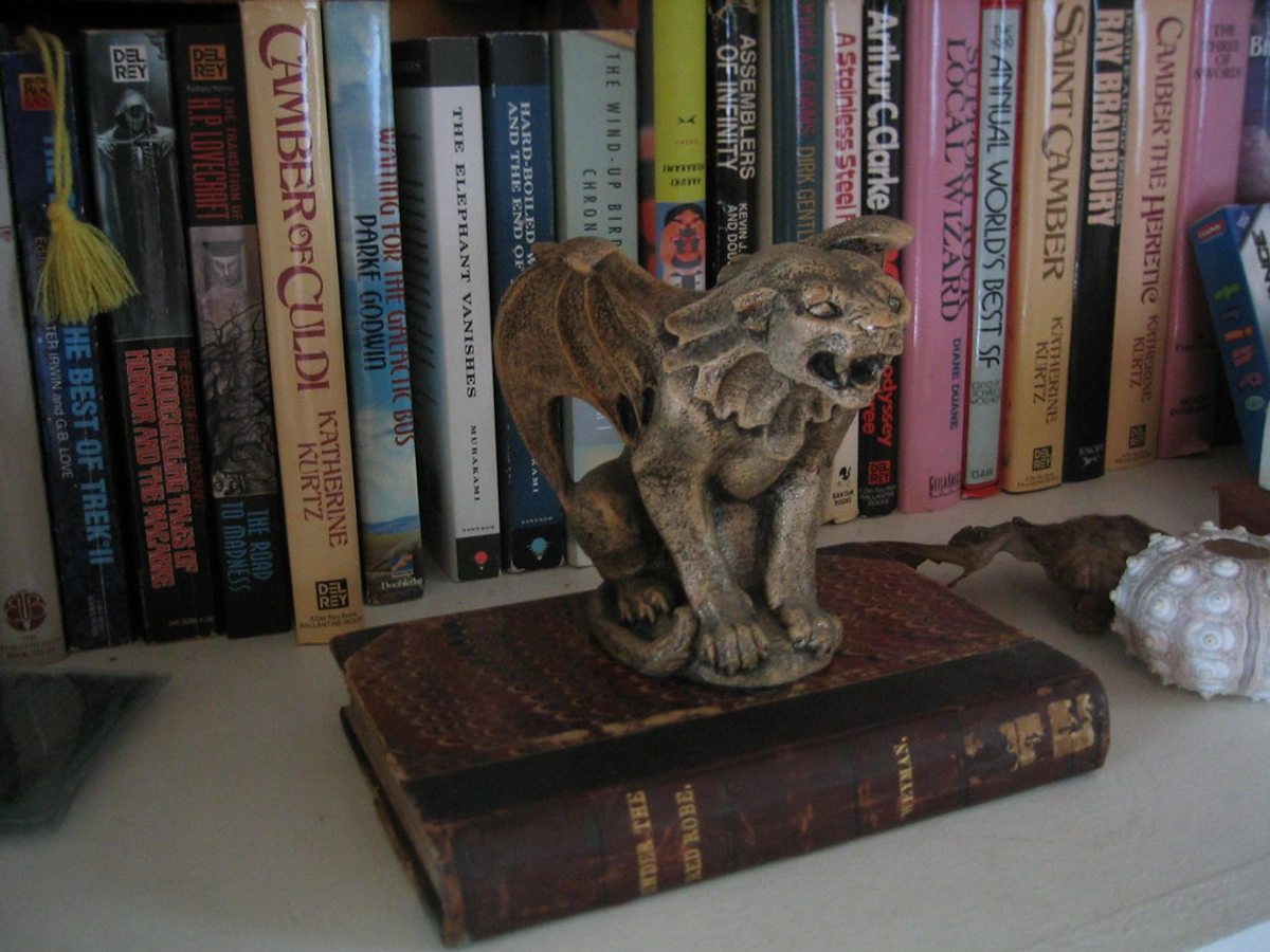 Small winged lion gargoyle perched on a bookshelf among various books.