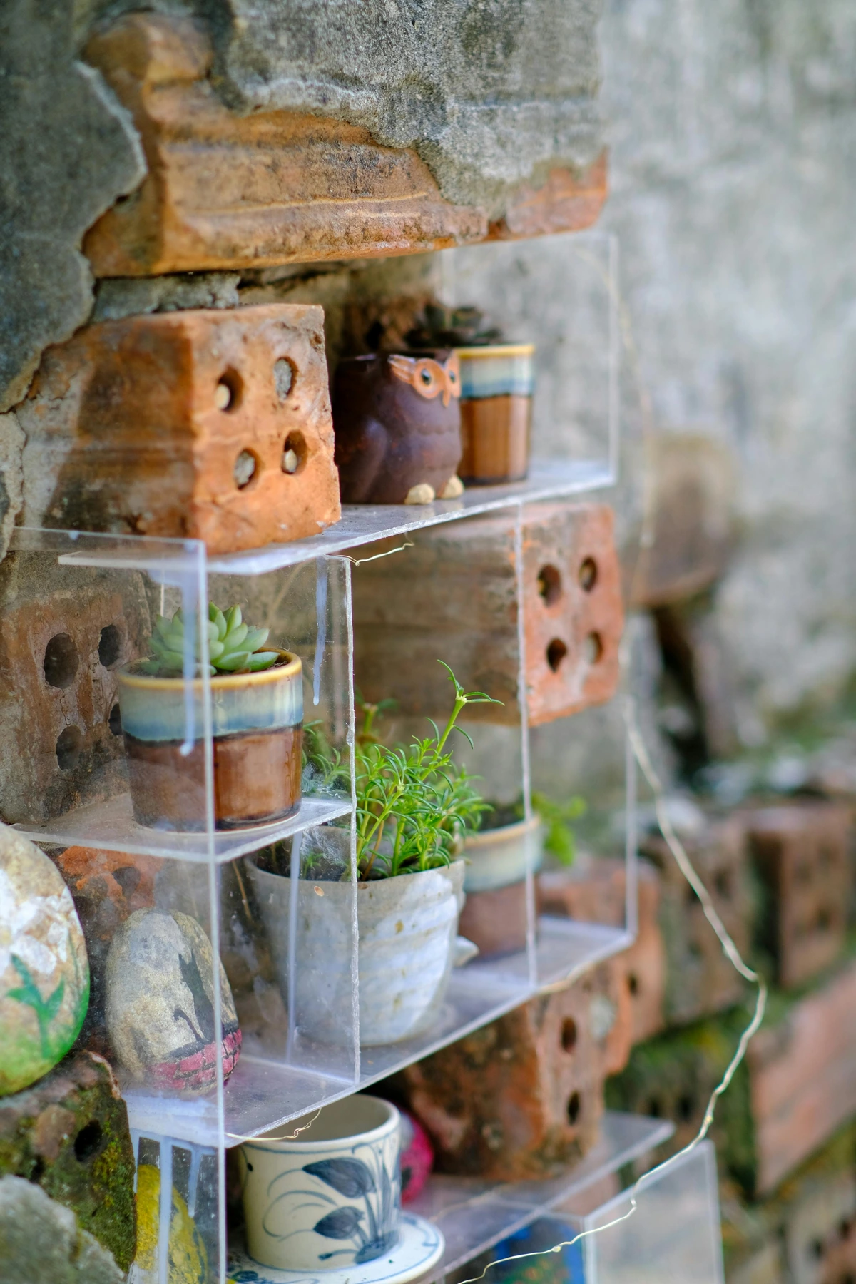 Rustic brick planters with succulents displayed on clear shelves against a textured wall.