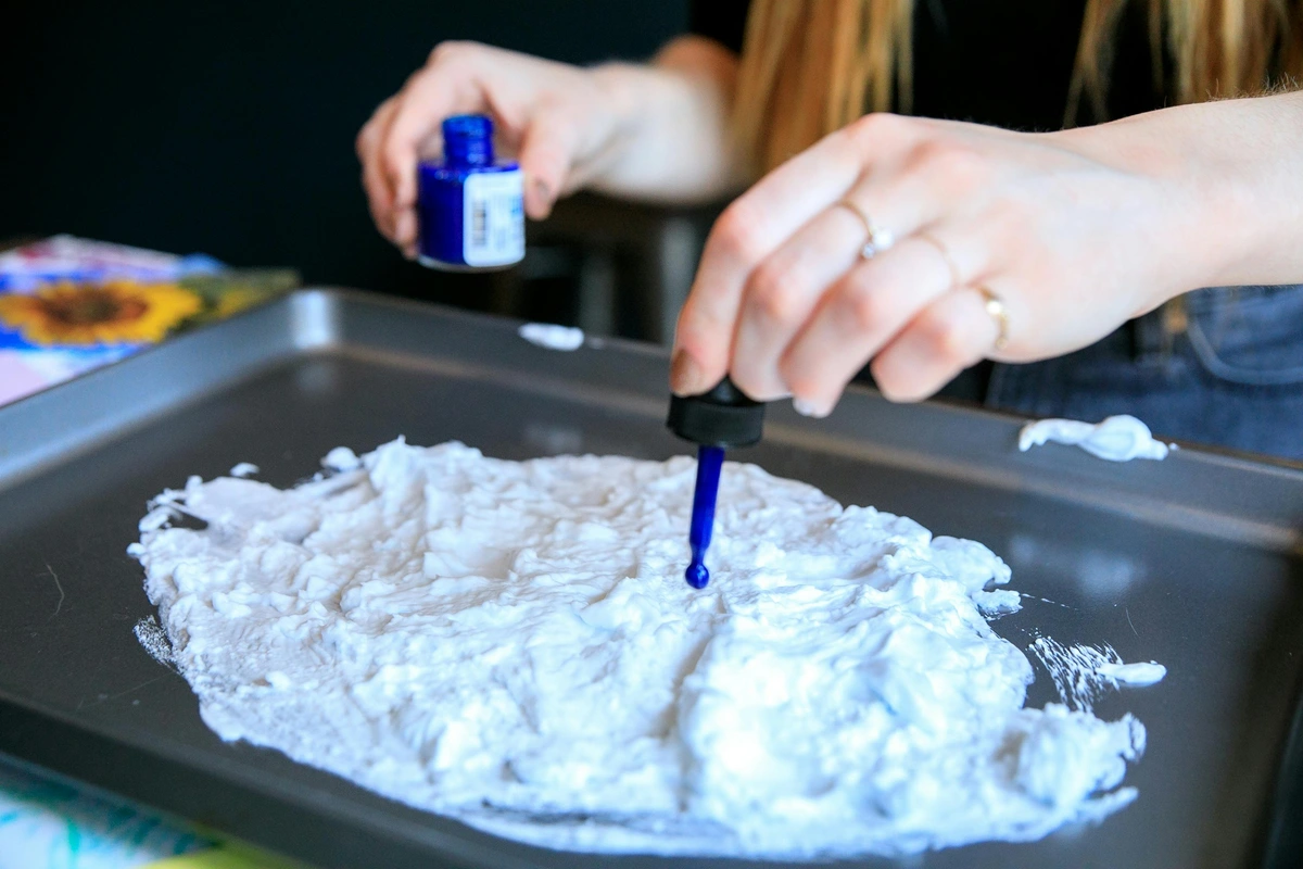 Close-up van een persoon die een pipet gebruikt om blauwe inkt toe te voegen aan witte verf op een dienblad, artistieke hobby.