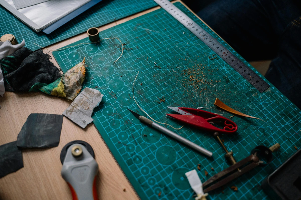 Sharp crafting tools including scissors, a craft knife, ruler, and rotary cutter laid out on a green cutting mat, ready for artwork preparation.