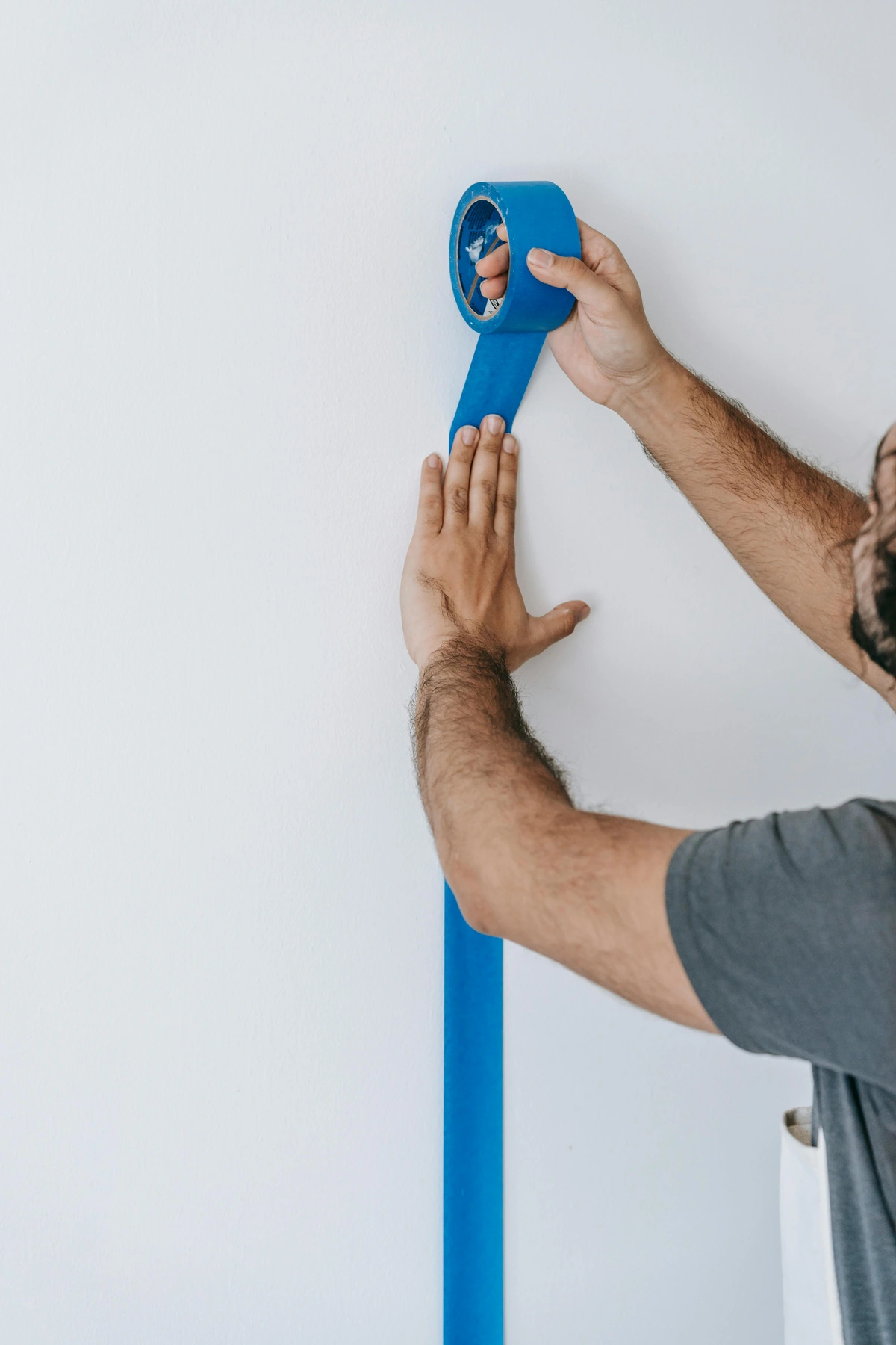 Man applying painter's tape to wall for crisp paint edges. Use this stock image for DIY painting tutorials and home improvement guides.