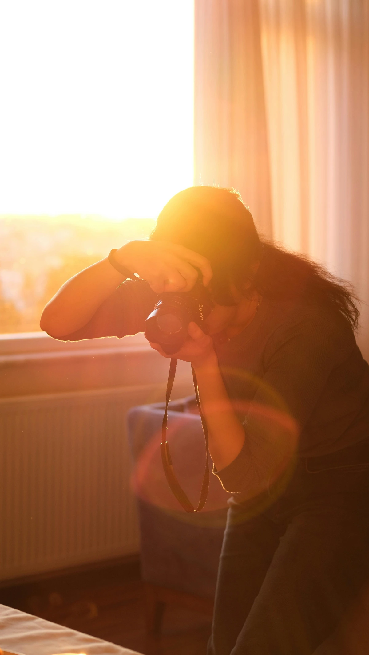 Woman photographing art at home with natural sunlight streaming through a window.