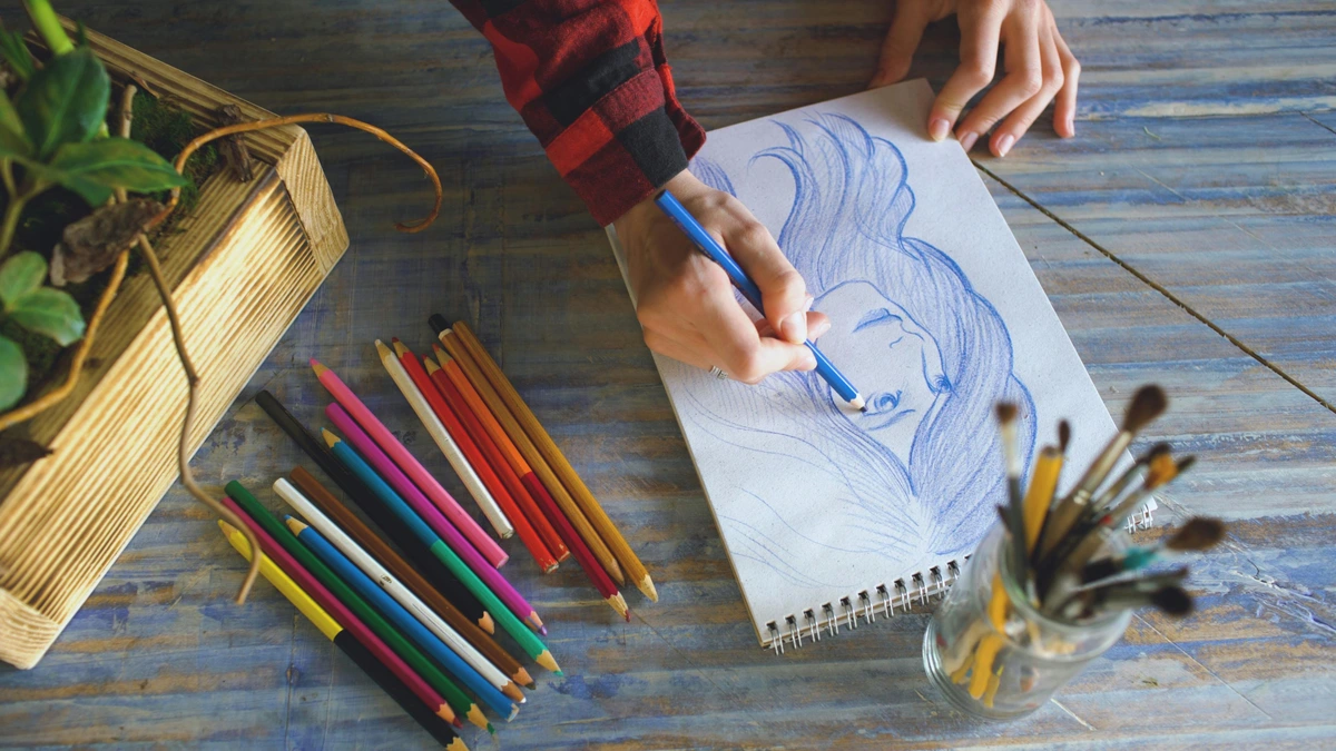 Person drawing a portrait with colored pencils on a wooden table