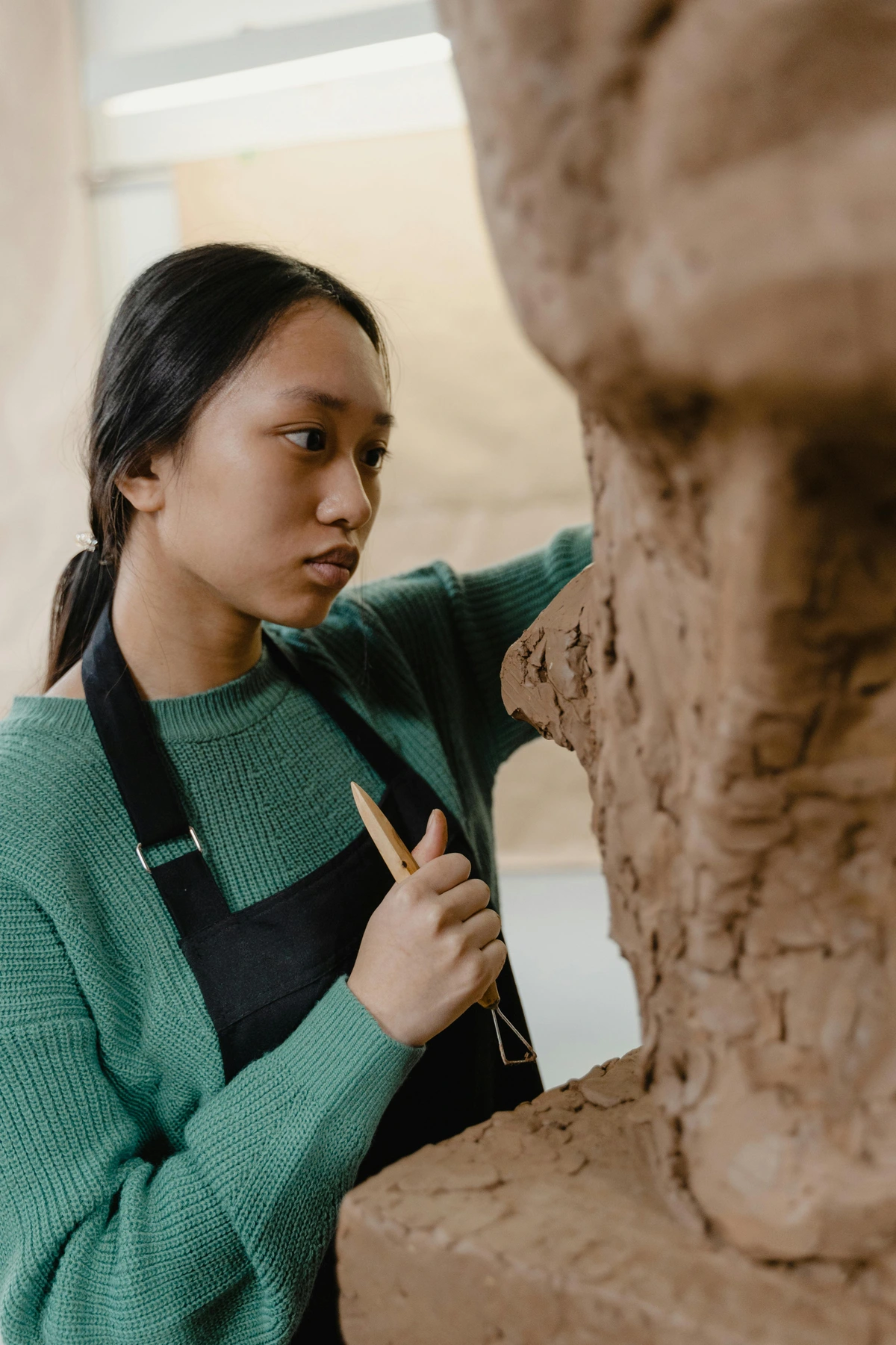 A female artist sculpting clay with a clay tool, focused and creative.