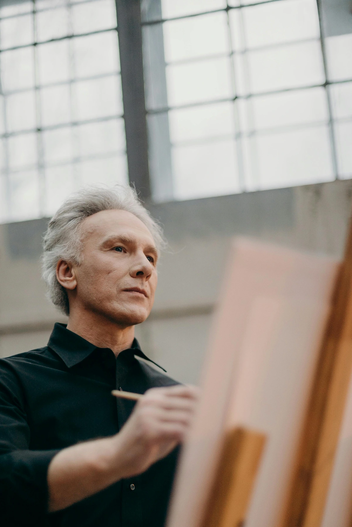 Man in black long sleeves painting on canvas in studio