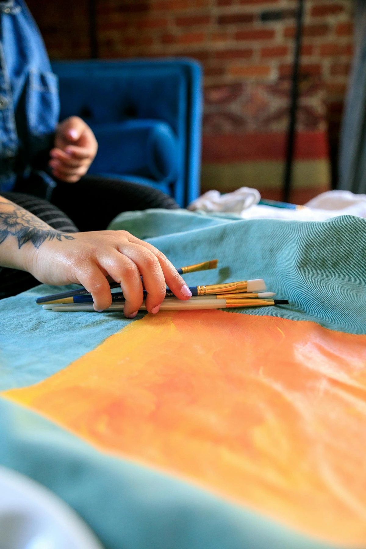 Close-up van getatoeëerde hand die verfkwasten vasthoudt over canvas kunstwerk