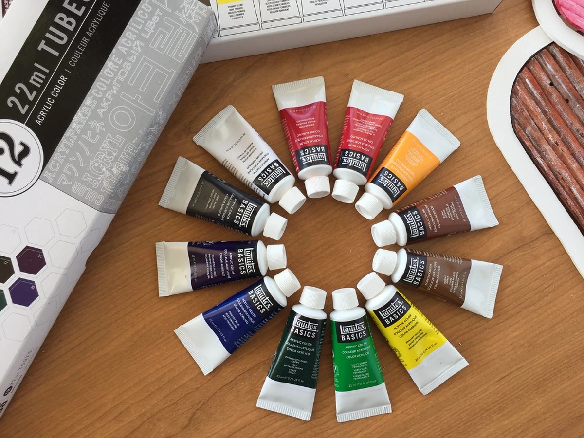 A collection of Liquitex Basics acrylic paint tubes arranged in a circle on a wooden surface.