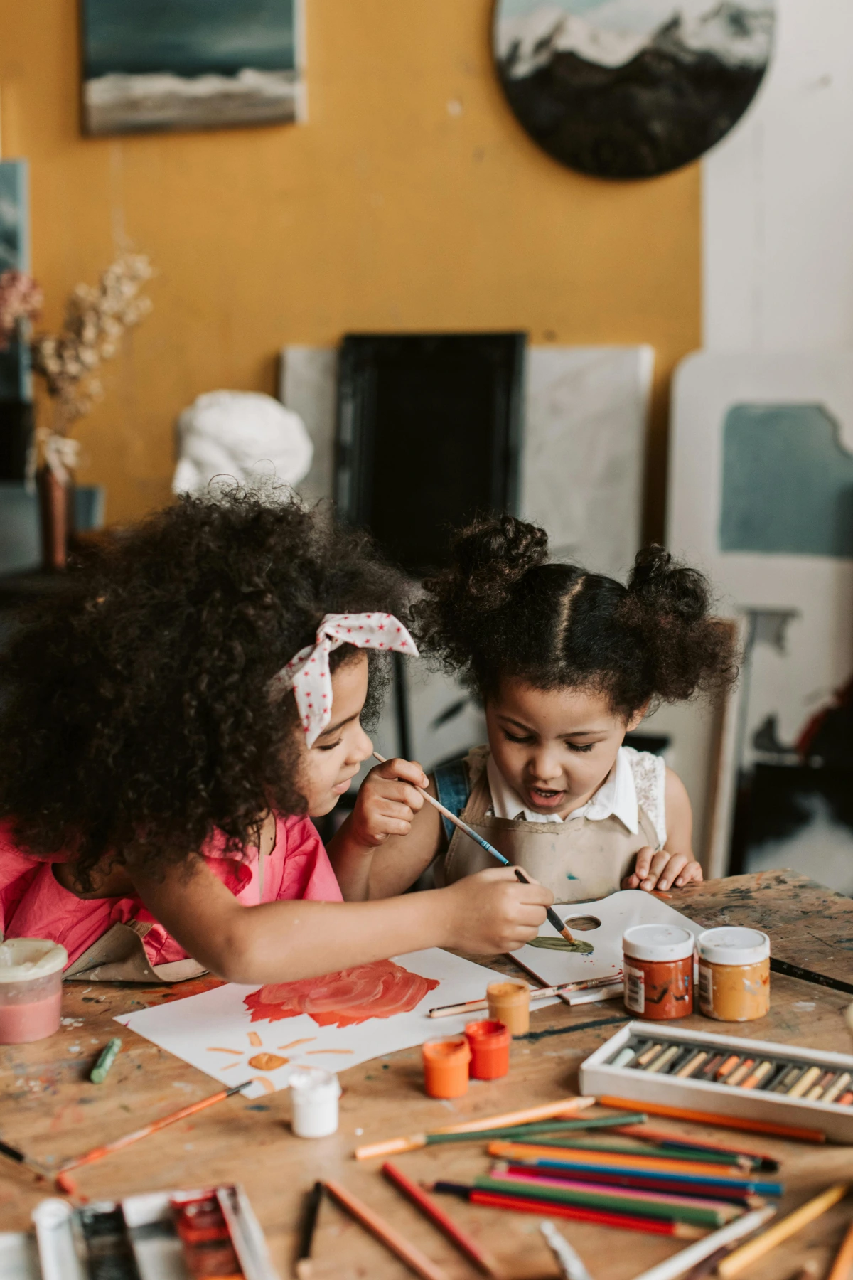 Two young girls engaged in a painting activity with brushes and art supplies on a table
