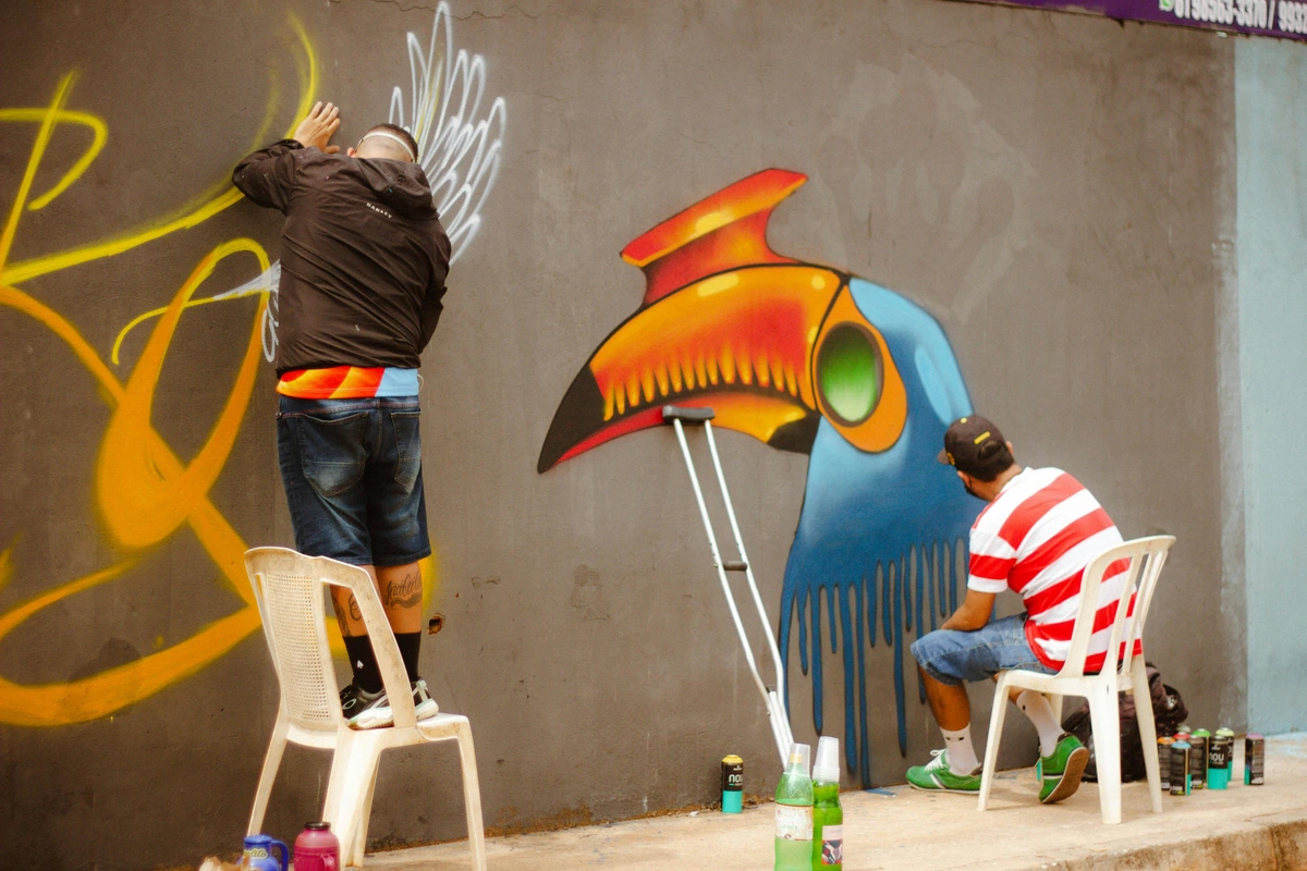 A graffiti artist applying paint to a vibrant toucan mural, showcasing accessible art initiatives in urban spaces. Free graffiti art transforming public environments into inclusive creative experiences.