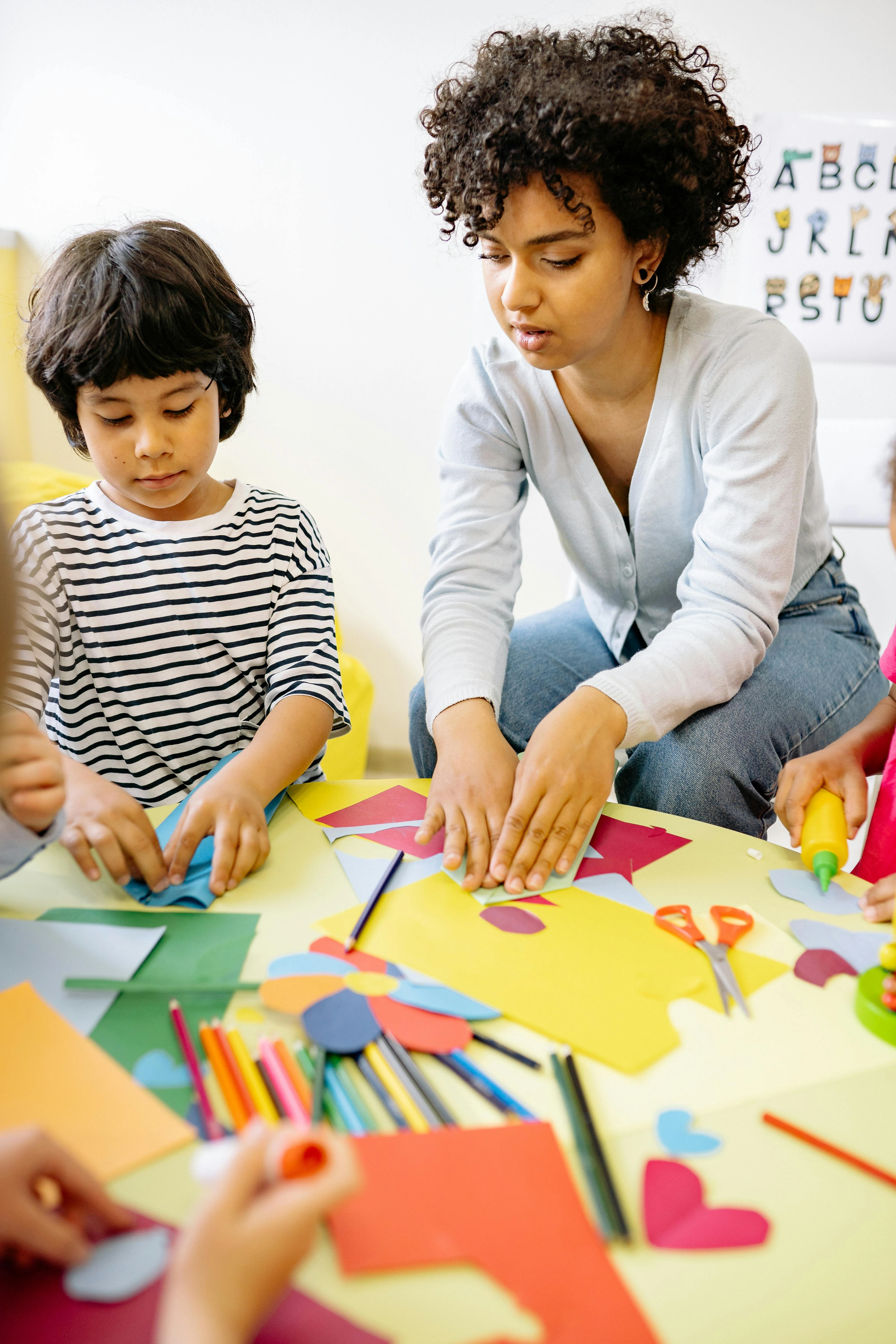 A woman teaching children arts and crafts in a classroom setting.