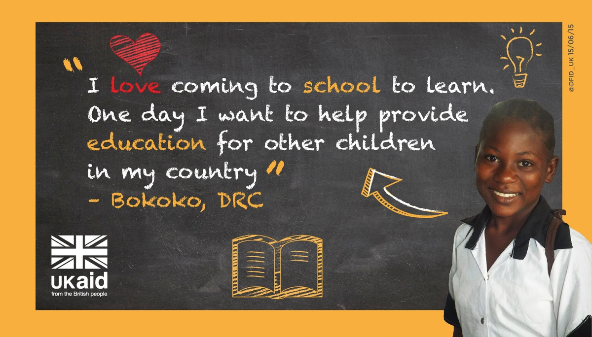 A young girl smiles as she stands in front of a chalkboard with a quote about her love for school and her dream to provide education for others in her country, Bokoko, DRC.