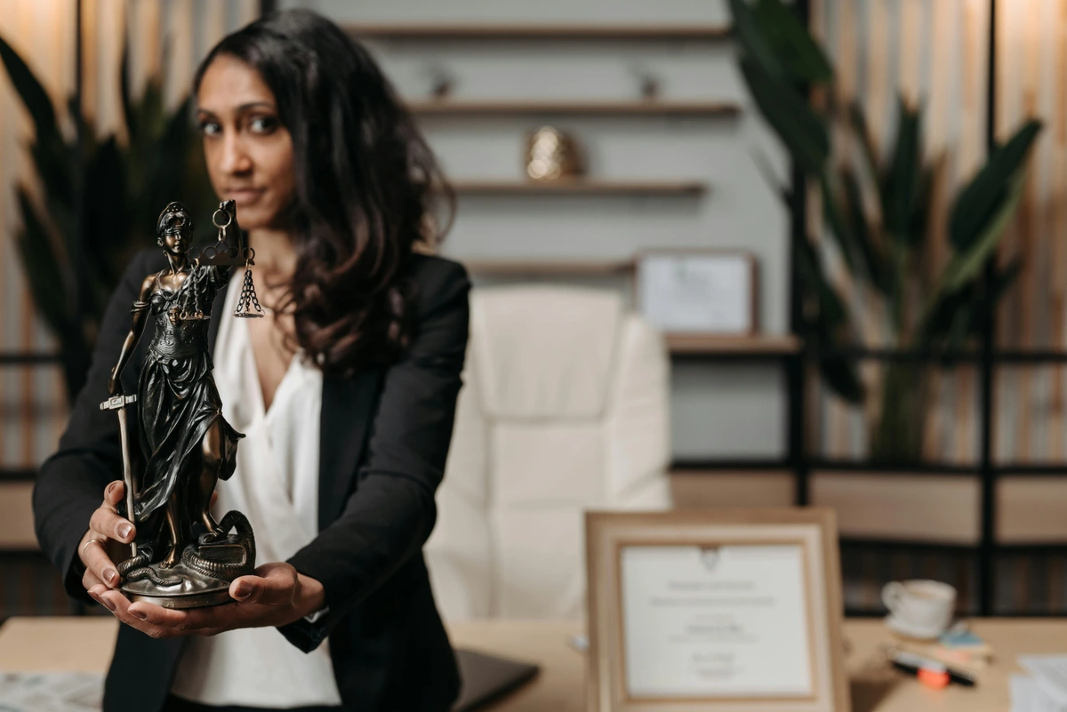 Woman in black blazer holding Lady Justice statue in office setting
