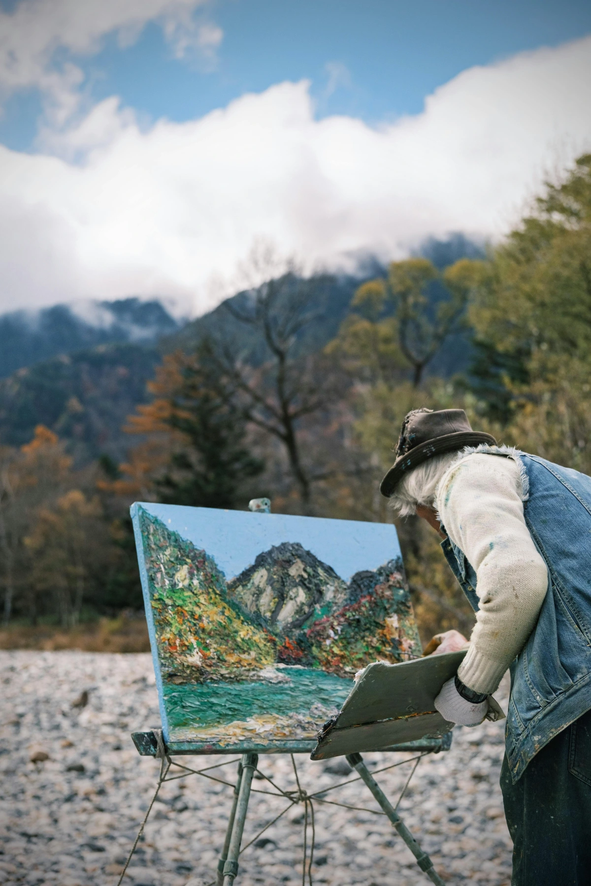 Artist painting a mountain landscape en plein air, showcasing a portable easel.