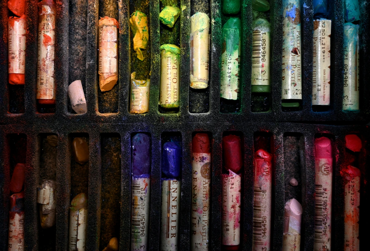 Close-up shot of a used set of Sennelier oil pastels in various colors, showcasing the texture and wear of the artist's materials.