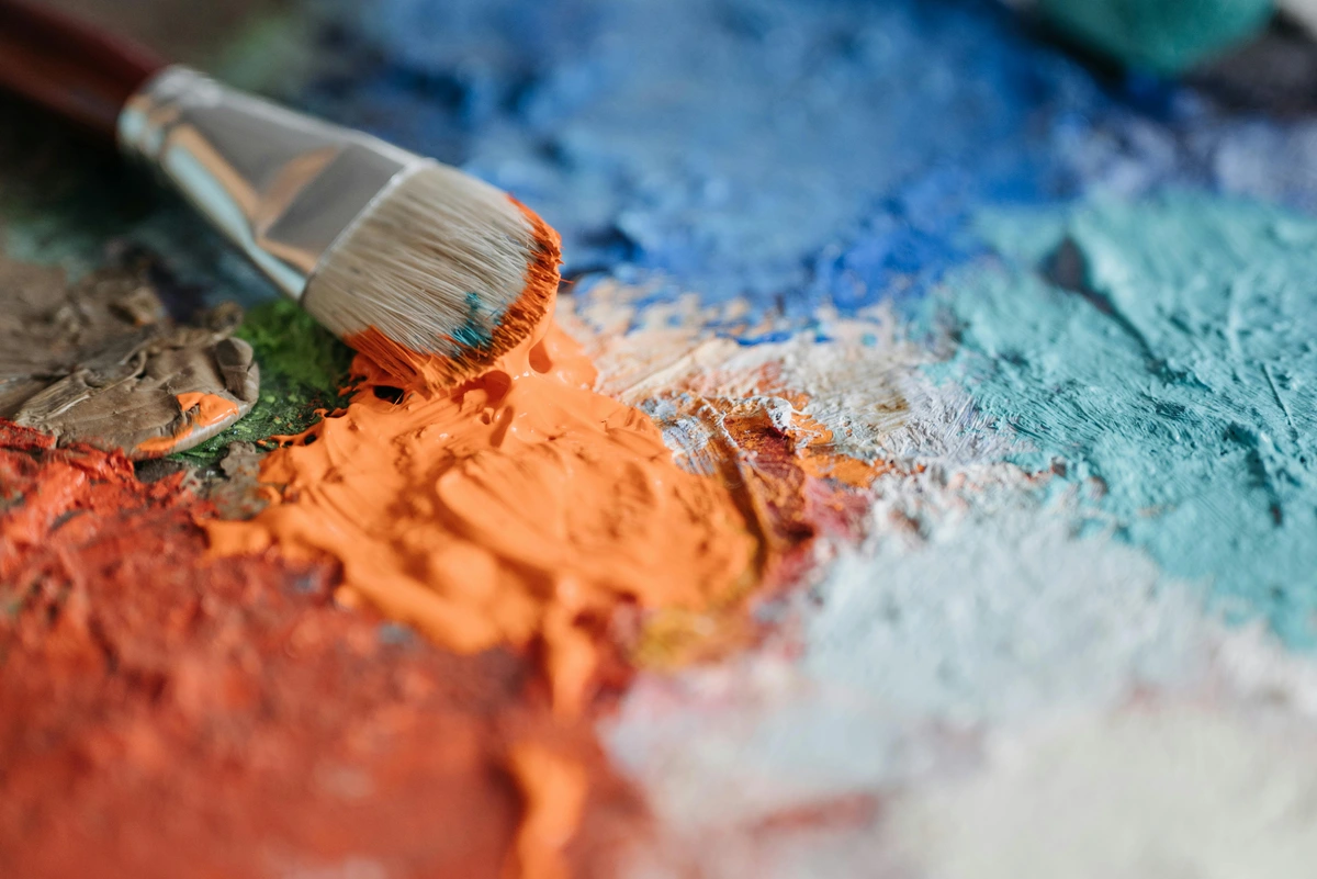 Synthetic paint brush lying on a surface with colorful paint smudges, showcasing various shades and textures | Free Stock Photo