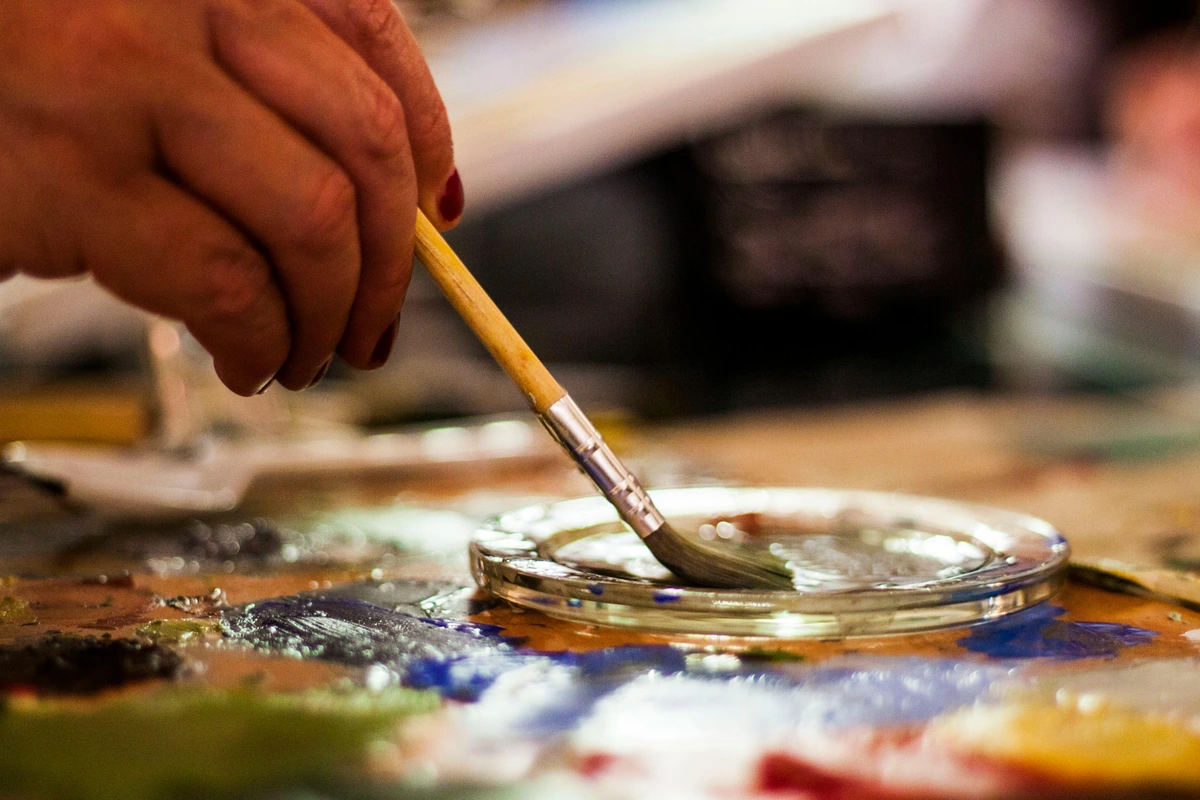 Person holding brown synthetic and gray natural art brushes for painting demonstration, highlighting brush differences