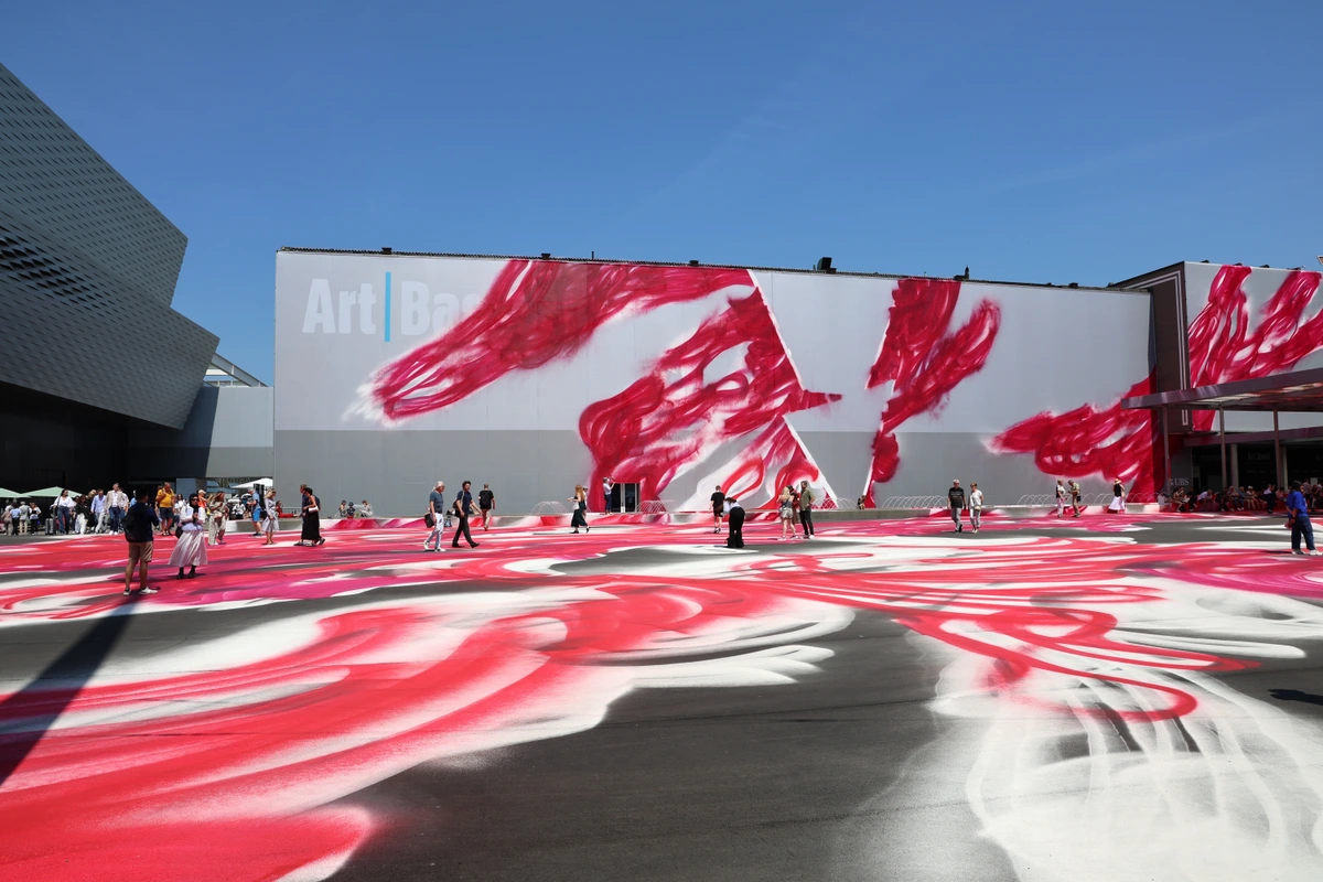 Messeplatz in Basel featuring Katharina Grosse's 'CHOIR' installation, with people walking on a vibrant red and white sprayed ground art.