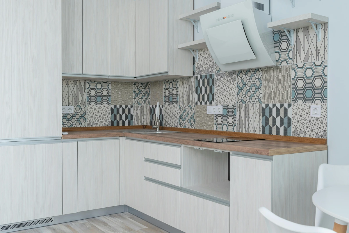 Modern white kitchen featuring a geometric patterned tile backsplash above the countertop and sink.