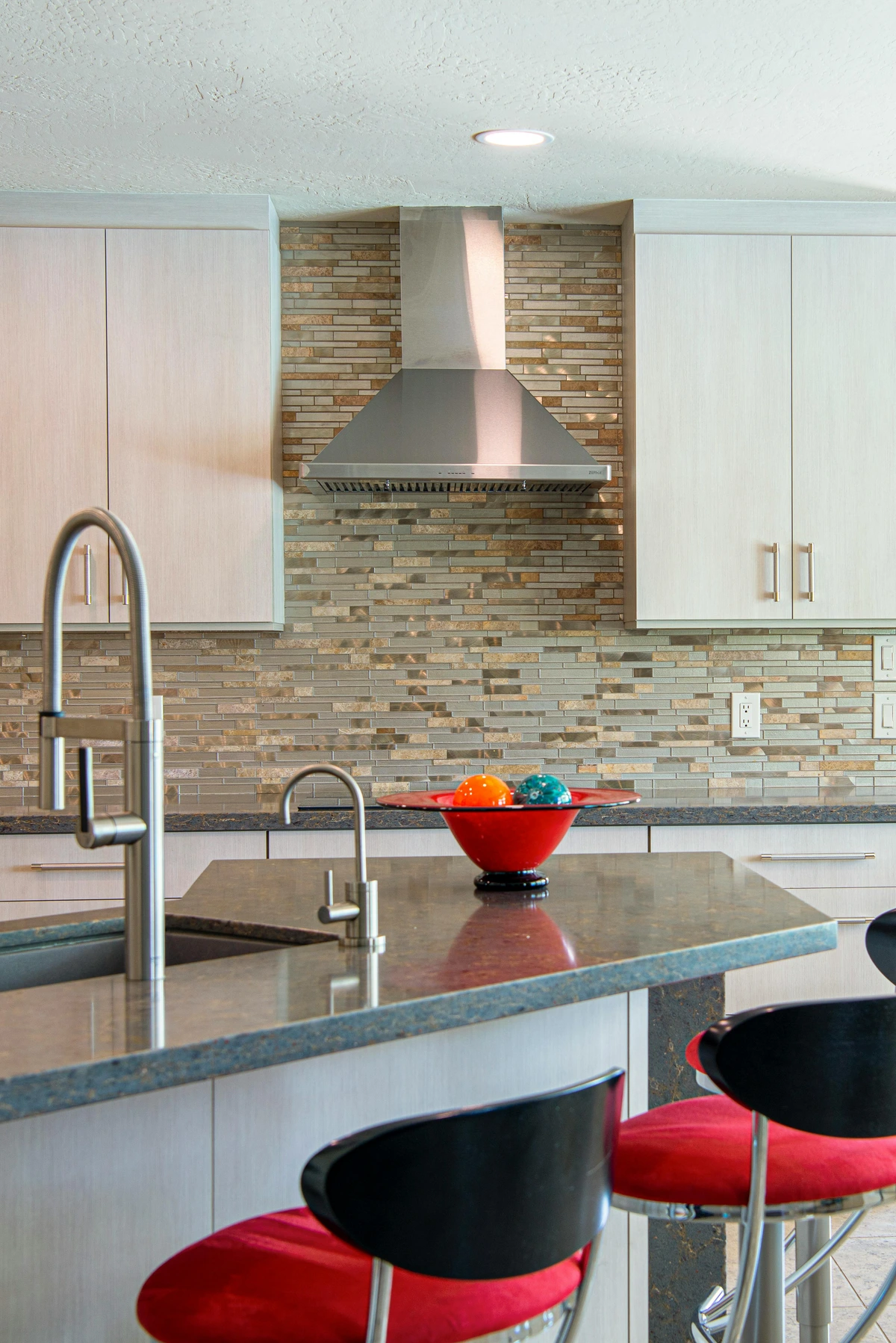 Modern kitchen with a decorative mosaic tile backsplash and a sleek stainless steel range hood.