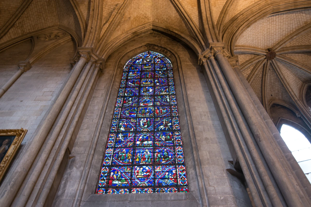 Stained glass window in Rouen Cathedral, showcasing intricate historical designs and vibrant colors.