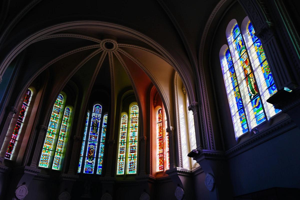 Interior view of gothic cathedral stained glass windows, showcasing intricate designs and vibrant colors filtering through the glass.