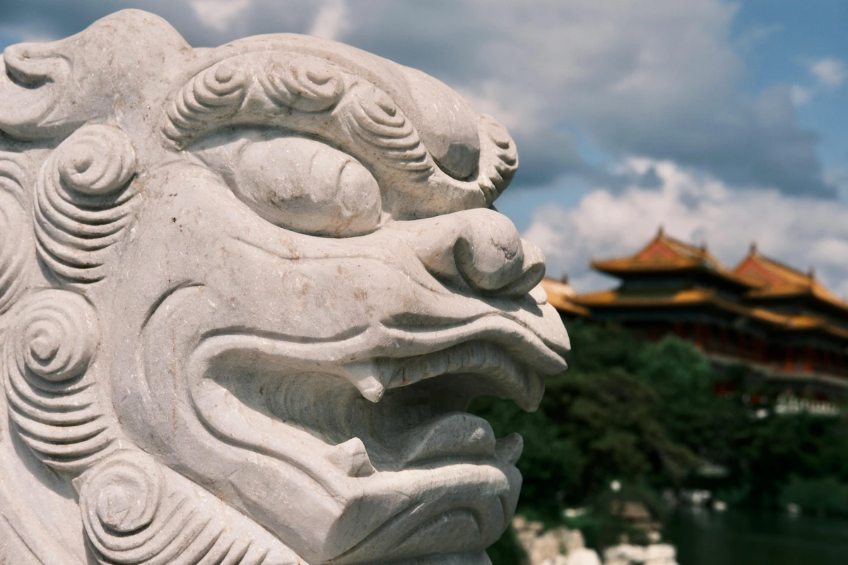Close-up of a white marble sculpture of a Chinese dragon's head, with traditional Chinese architecture in the blurred background.