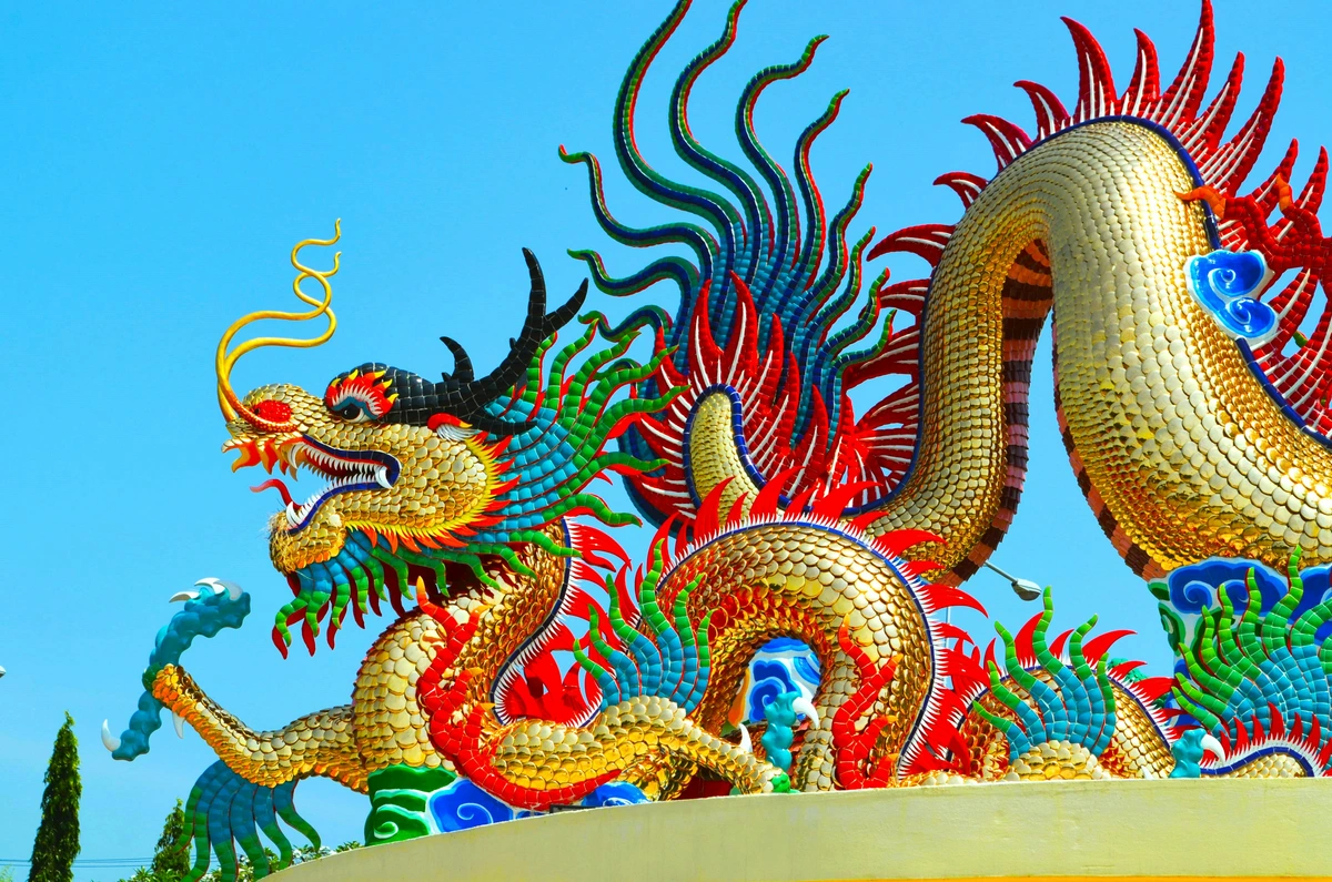 A vibrant, golden Chinese dragon statue with intricate details, set against a clear blue sky, symbolizing power, wisdom, and fortune.