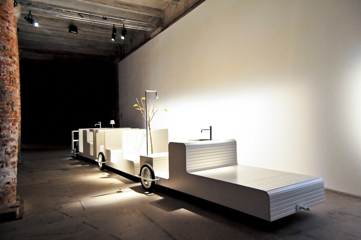Venice Architecture Biennale 08 installation featuring a modular white structure resembling a train with sinks, lamps, and a decorative tree.