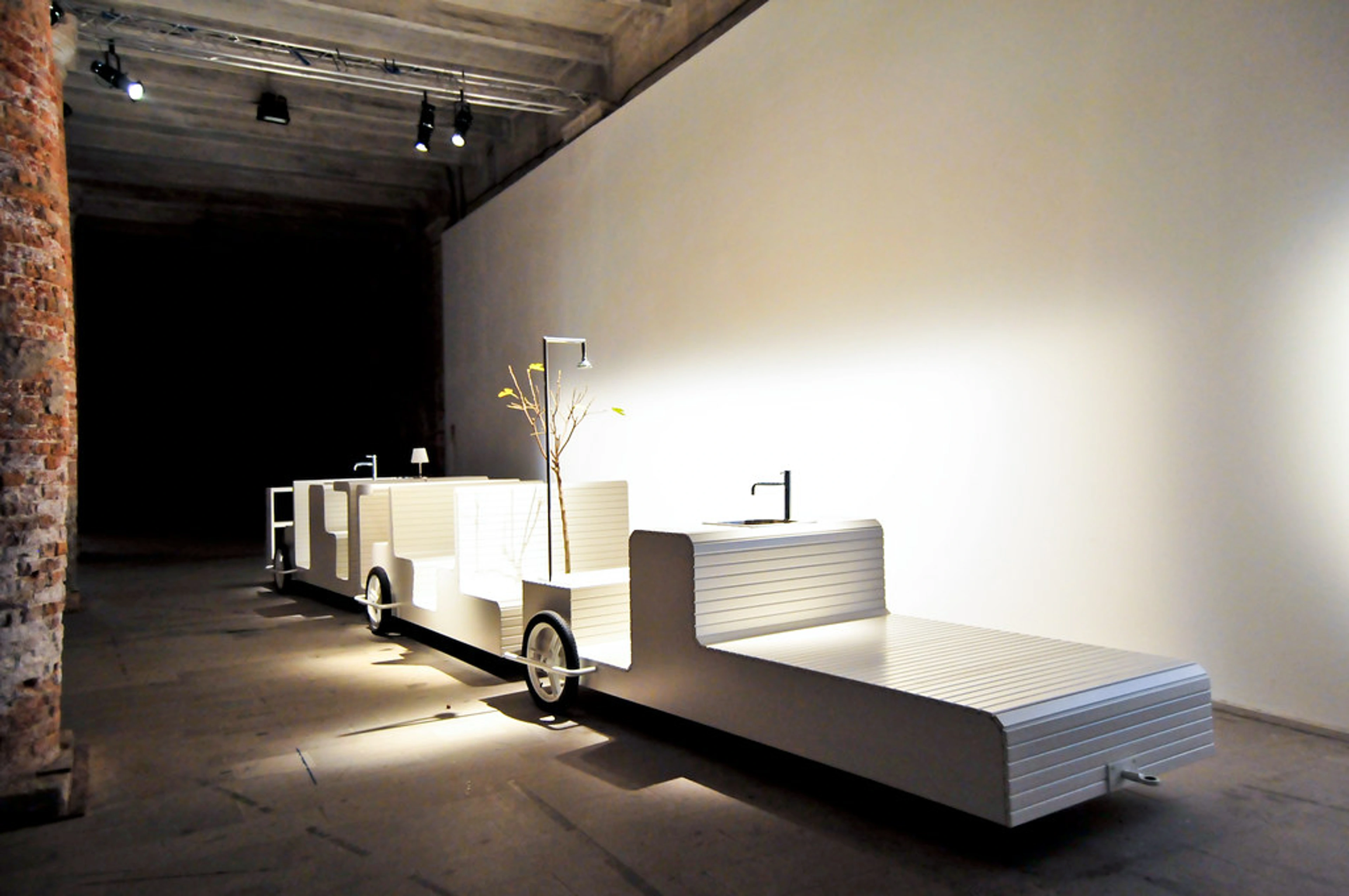 Venice Architecture Biennale 08 installation featuring a modular white structure resembling a train with sinks, lamps, and a decorative tree.