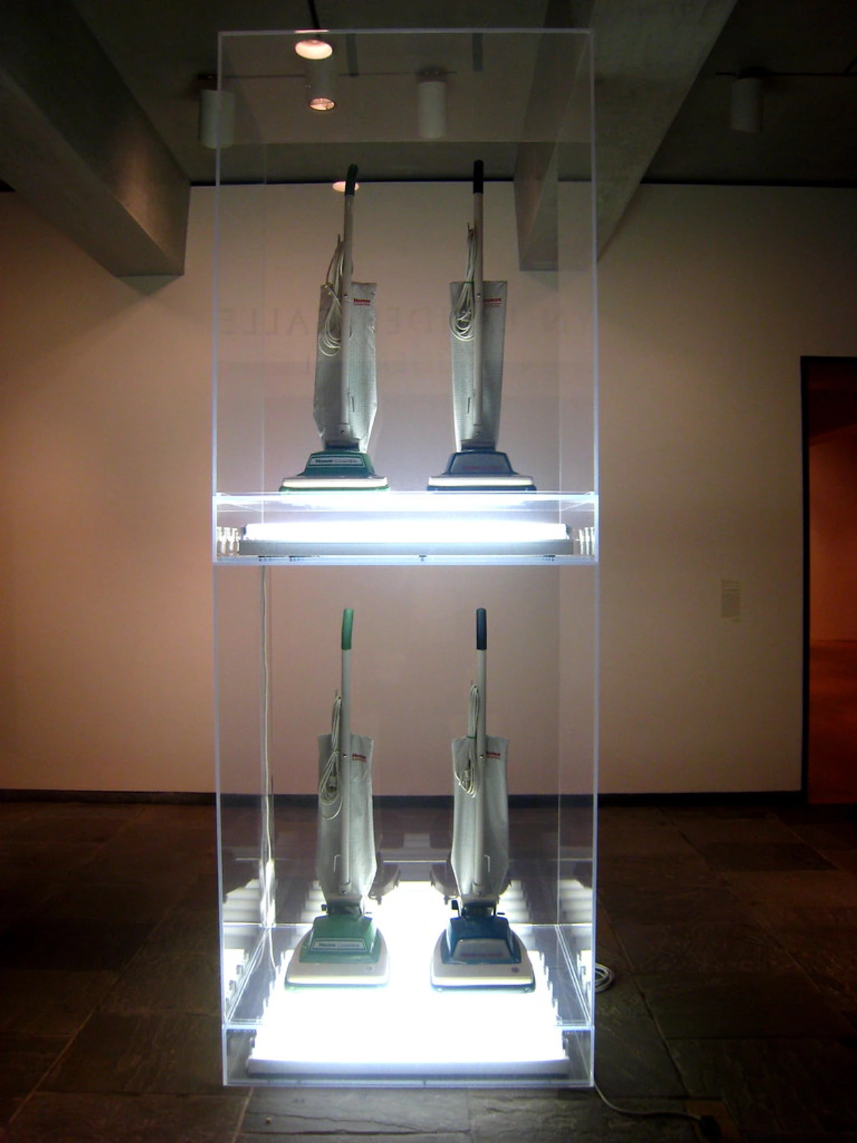 Jeff Koons vacuum cleaners displayed in a glass case with bright lighting.