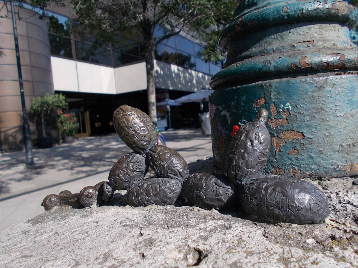Mihaly Kolodko's bronze sculpture of a balloon dog made of bones, placed on a stone pedestal in front of a modern building.