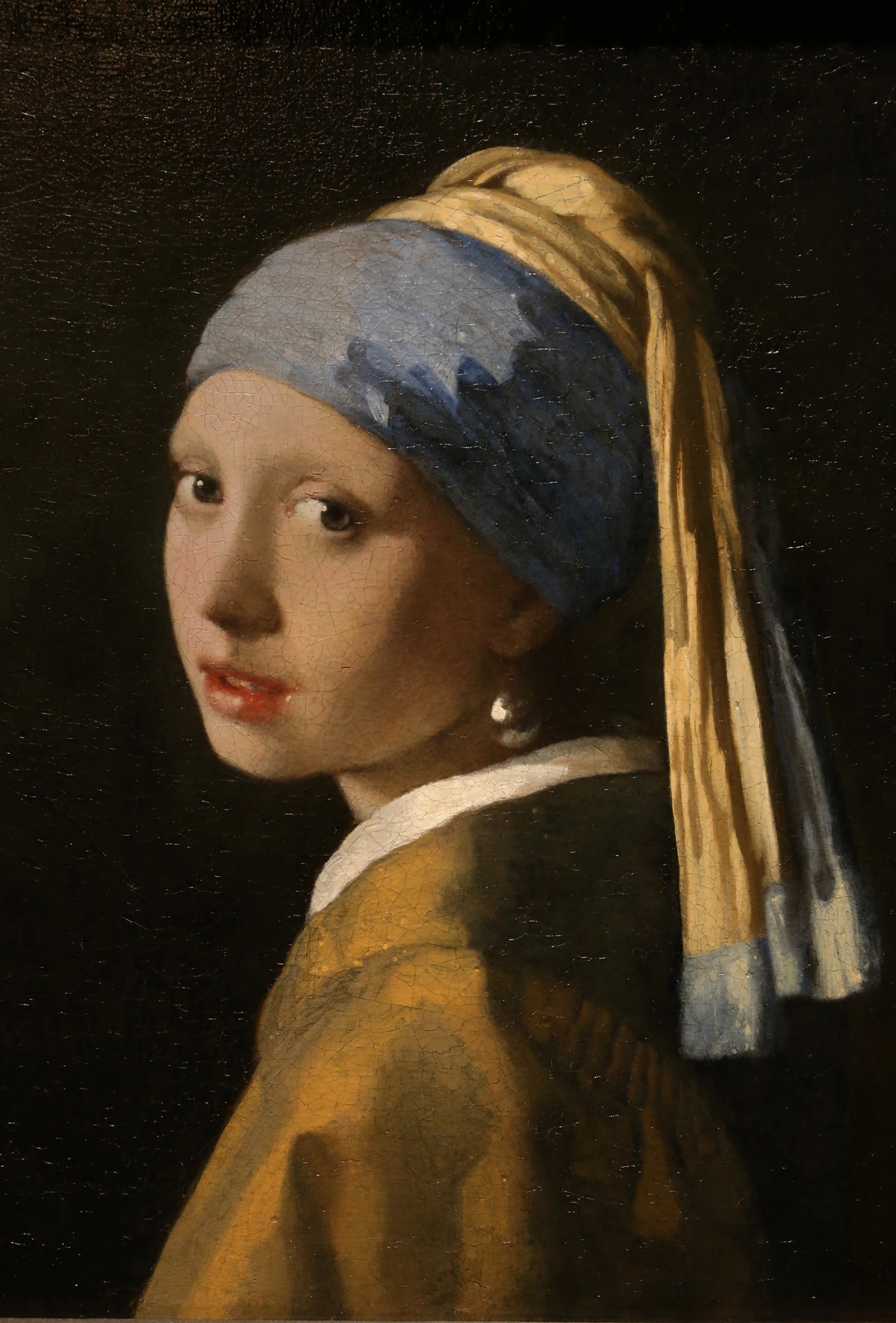 Johannes Vermeer's iconic painting 'Girl with a Pearl Earring' (c. 1665), featuring a young woman in a blue and gold turban and a large pearl earring, looking over her shoulder against a dark background.