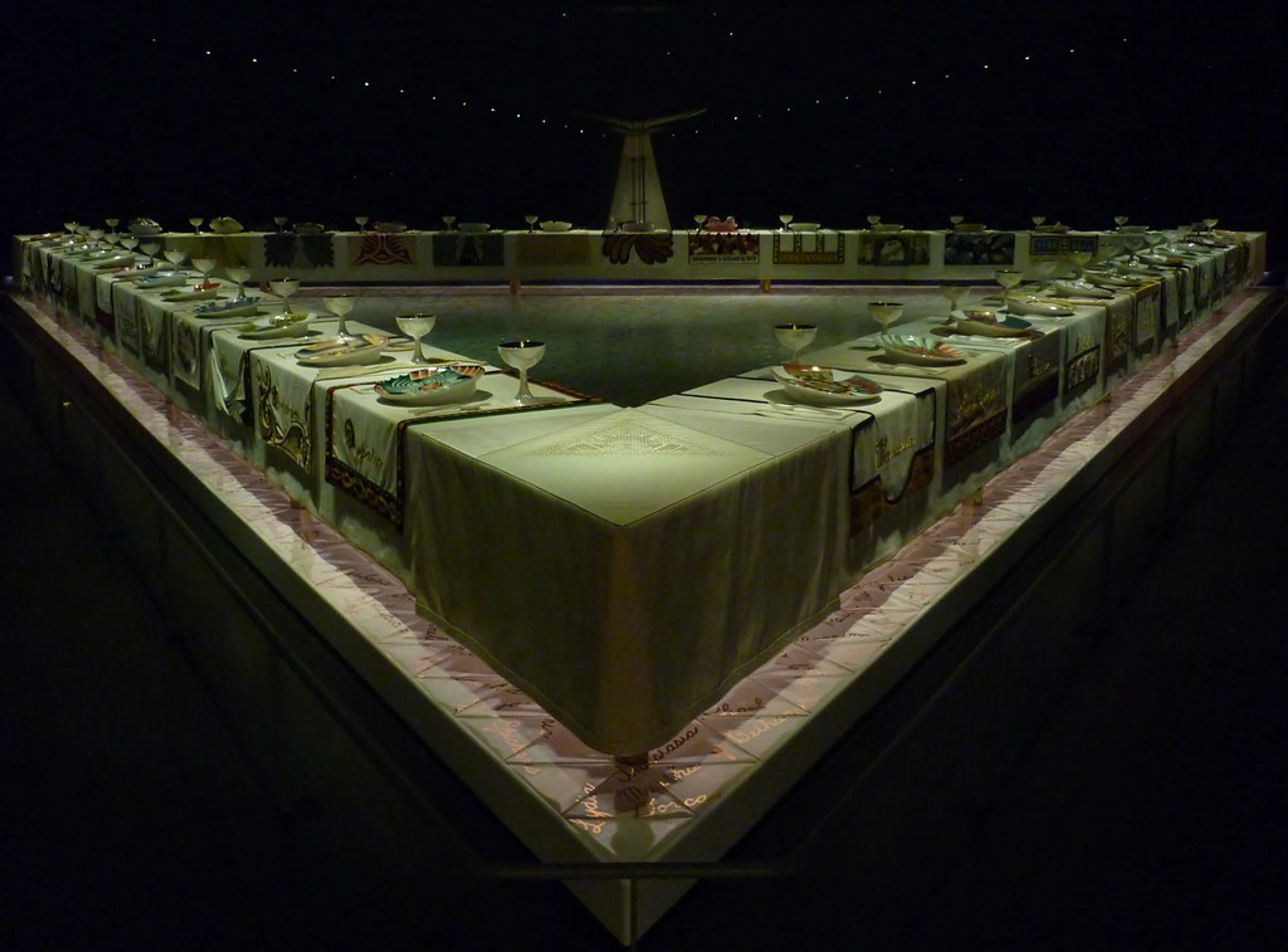 Judy Chicago's The Dinner Party installation at the Brooklyn Museum, featuring a triangular table with elaborate place settings.
