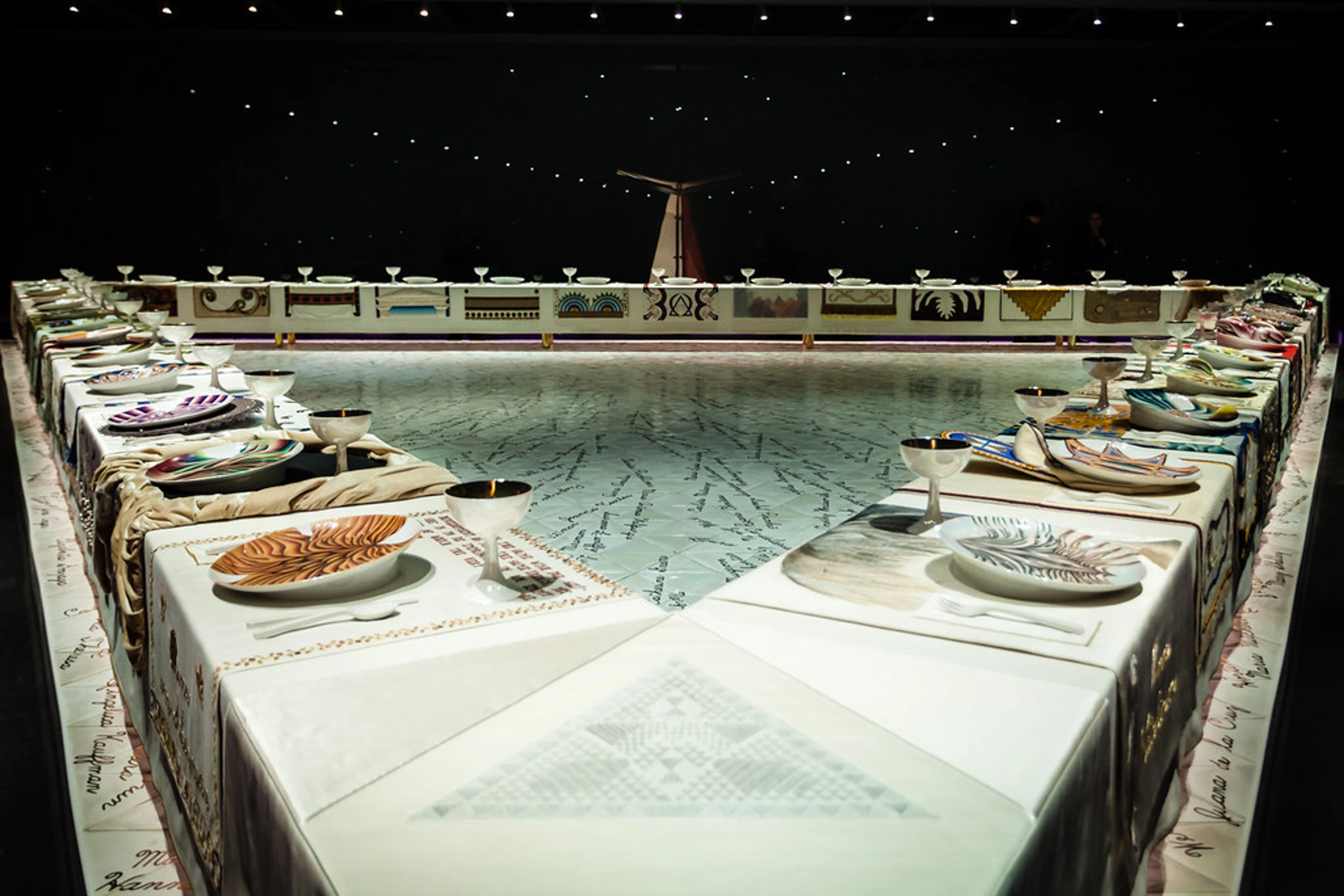 A triangular table setting for Judy Chicago's iconic feminist art installation, The Dinner Party, featuring elaborate place settings with unique plates and goblets.