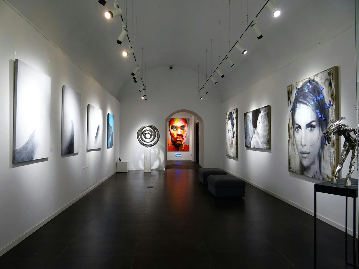 Modern art exhibit showcasing intellectual artwork in a well-lit gallery with sculptures, colorful faces, and everyday object installations