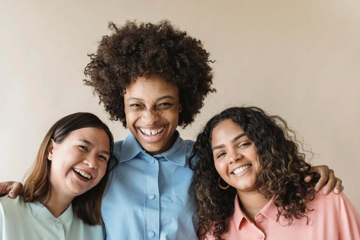Three diverse women laughing together in a moment of shared happiness, representing universal human experiences through art