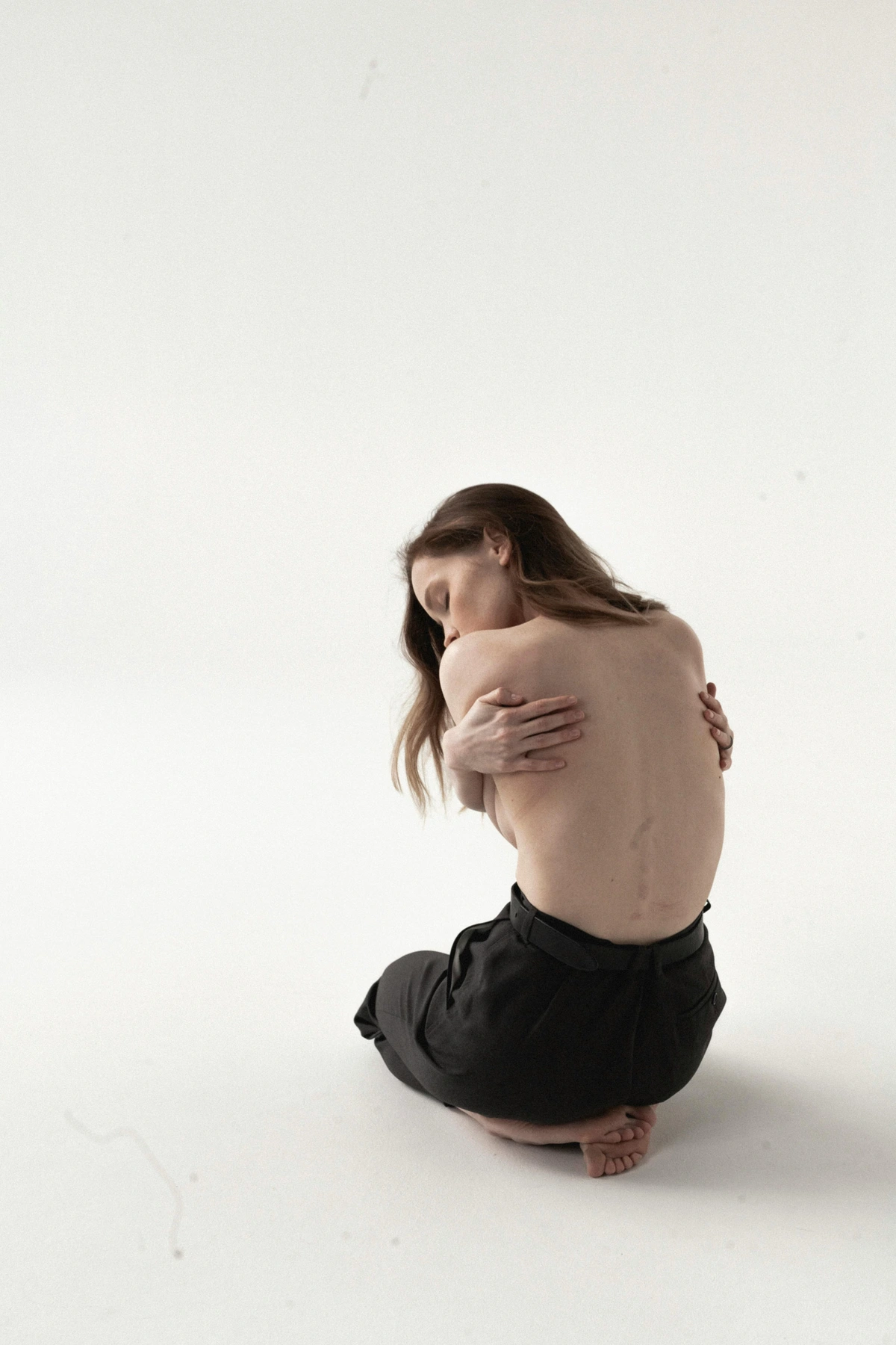 Shirtless woman sitting and embracing herself, representing Jungian female archetypal imagery of vulnerability and strength.