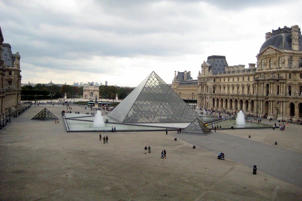 A glass pyramid at the center of the Cour Napoléon courtyard in the Louvre Museum in Paris, surrounded by elegant buildings with classical French architecture.