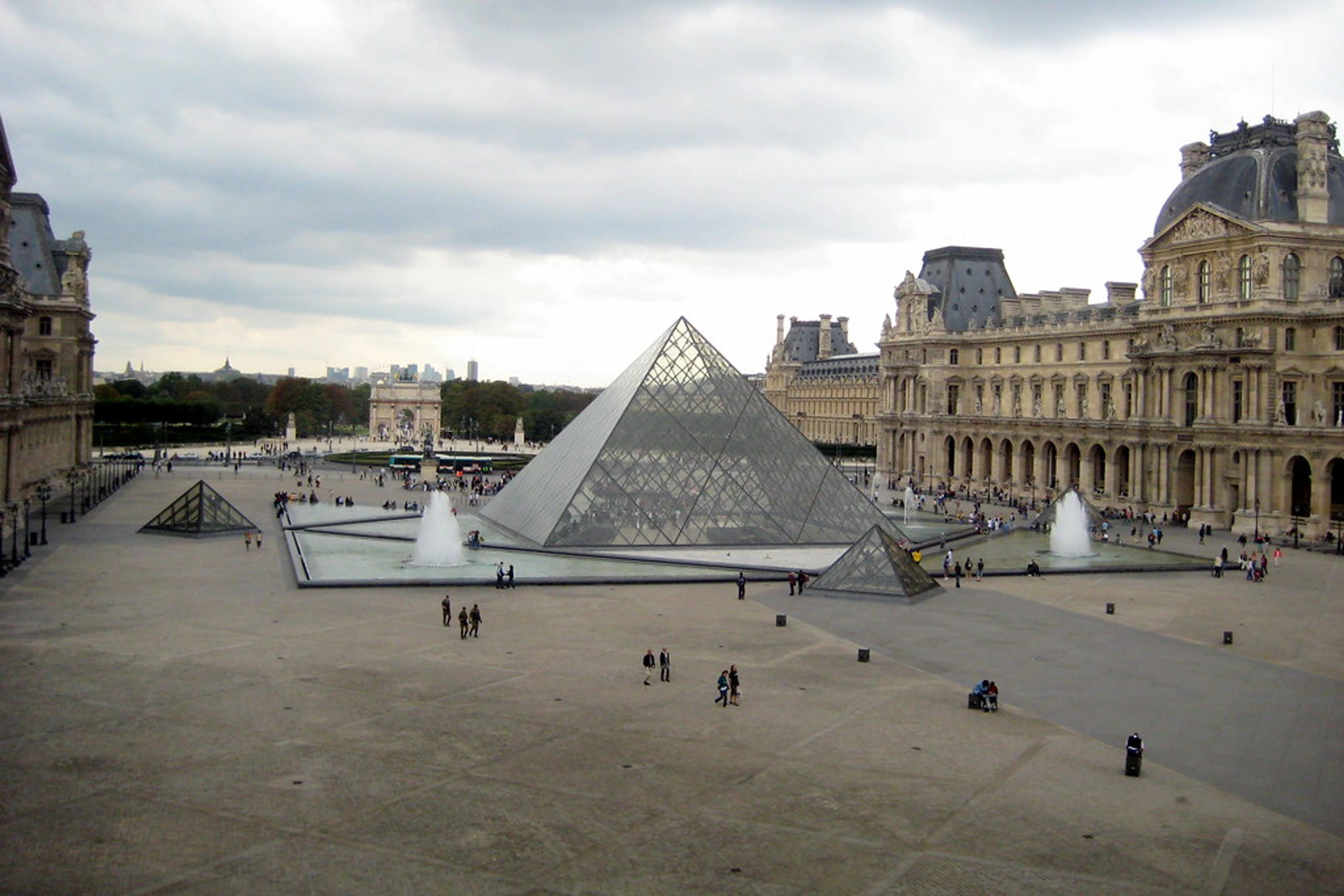 A glass pyramid at the center of the Cour Napoléon courtyard in the Louvre Museum in Paris, surrounded by elegant buildings with classical French architecture.