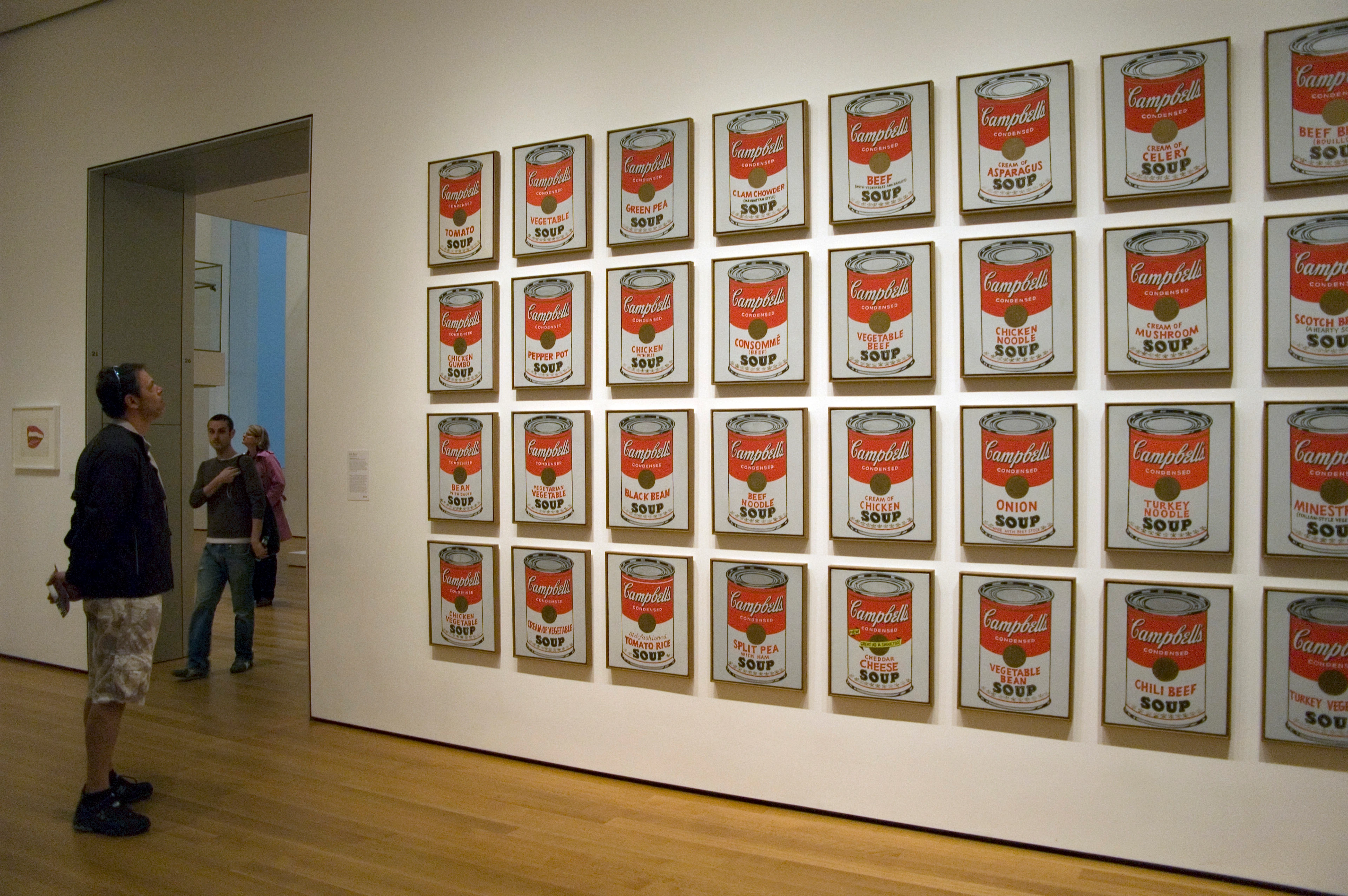 Andy Warhol's Campbell's Soup Cans artwork displayed in a museum gallery with visitors observing.