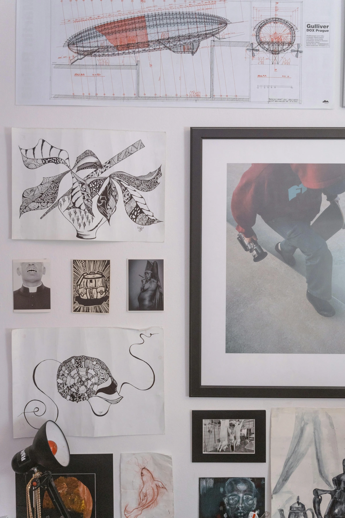 A diverse collection of artworks, including drawings, prints, and photographs, arranged on a white wall to create a gallery wall effect.