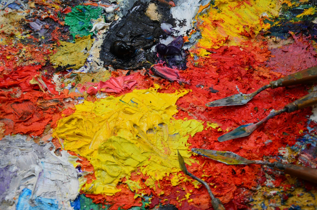 Close-up of a painter's palette covered in thick, vibrant oil paints and artfully arranged palette knives, showcasing rich textures and colors.