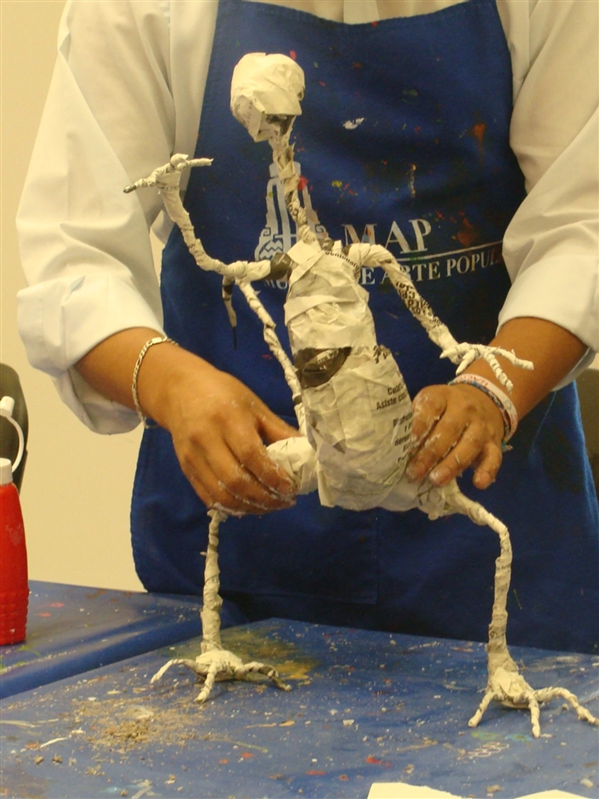 A person's hands working on a paper mache sculpture, showing the wire armature underneath.